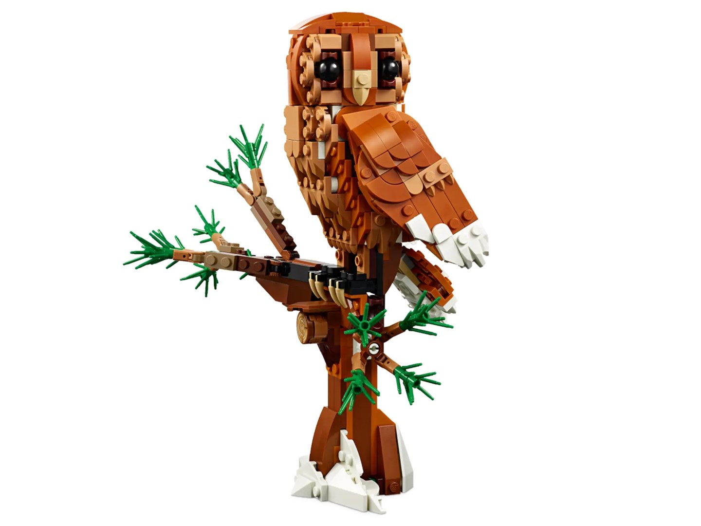 Un gufo Lego è seduto su un ramo Lego. Il gufo è marrone e bianco. L'albero ha foglie verdi.