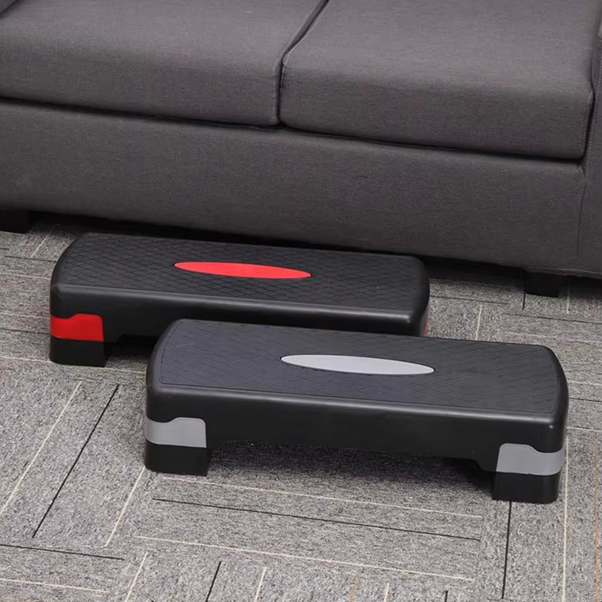 Dos plataformas de escalón negras con acentos de color. Una tiene rojo, la otra gris. Sofá gris en el fondo, sobre un suelo estampado.