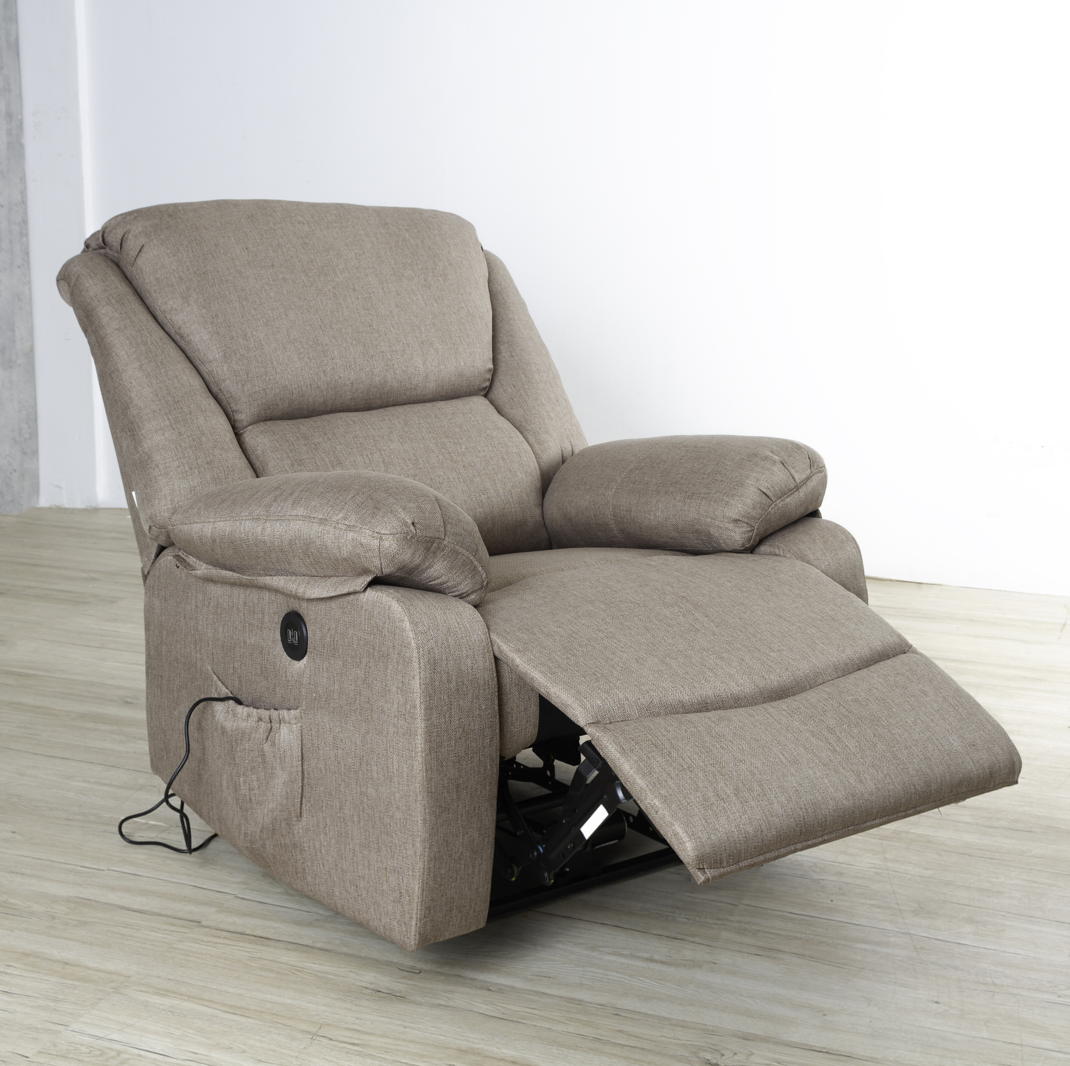 Sillón reclinable beige con reposapiés extendido sobre suelo de madera clara, contra pared blanca.