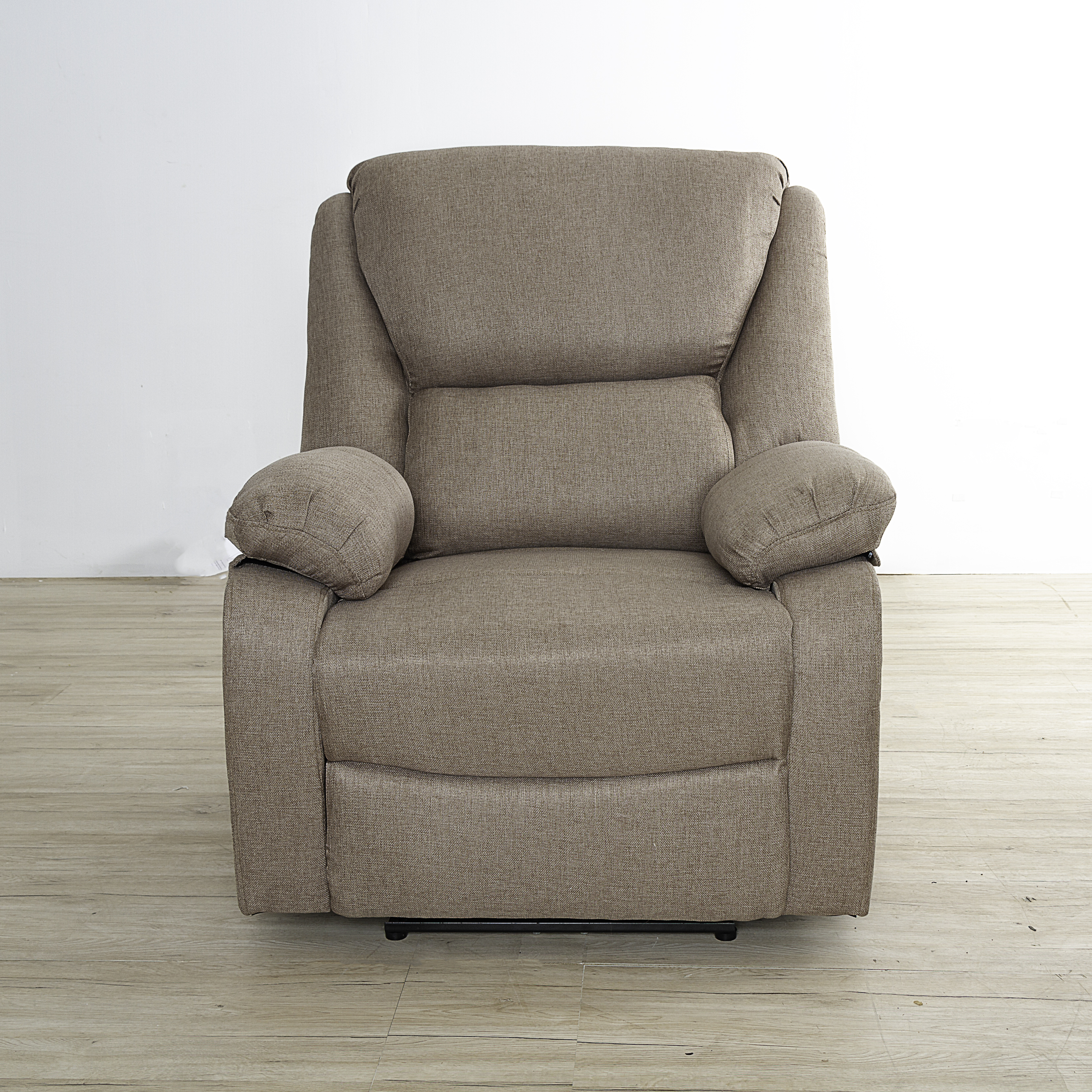 Un sillón reclinable marrón sobre un suelo de madera contra una pared blanca. El sillón tiene reposabrazos y reposacabezas.