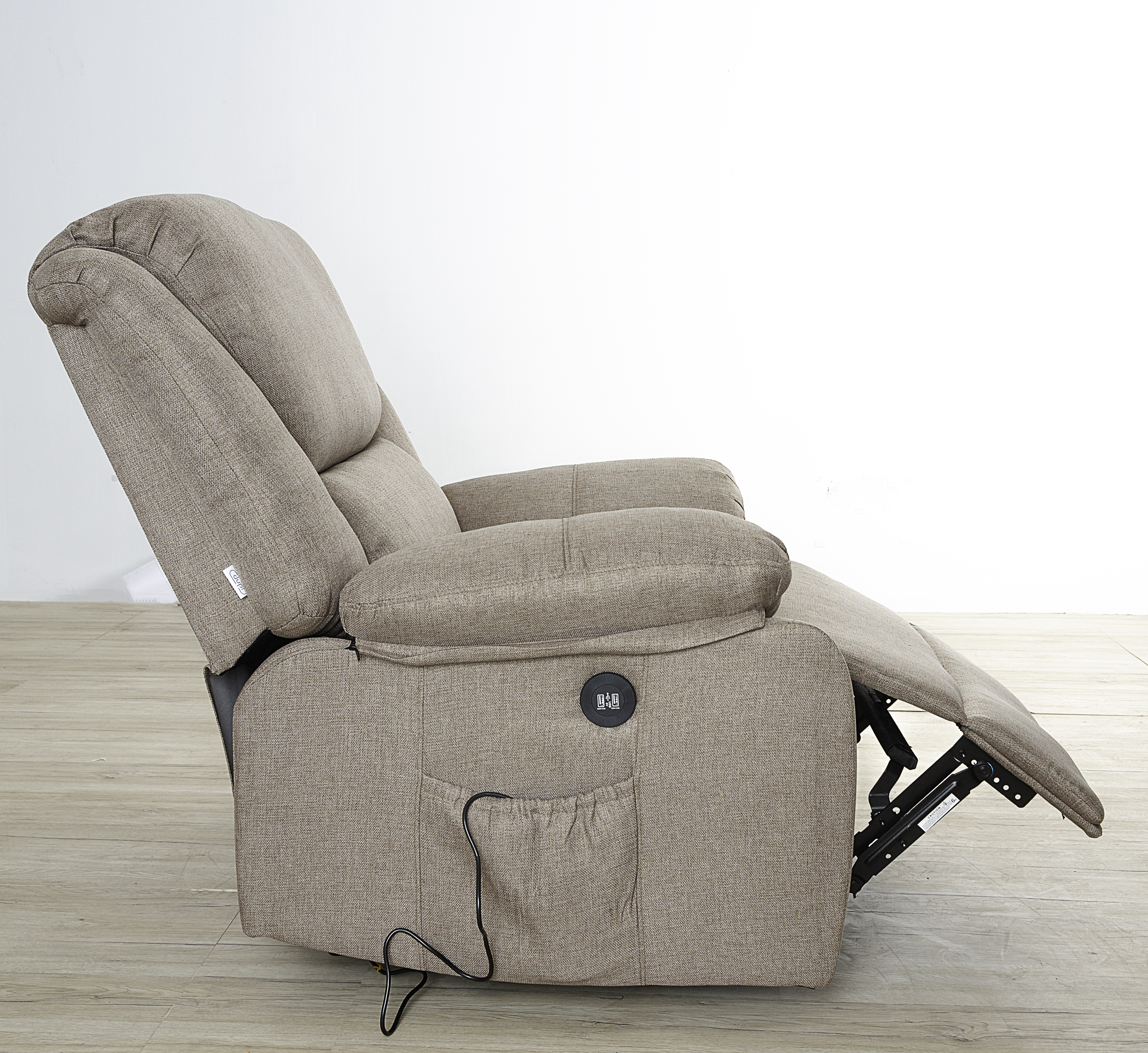Sillón reclinable beige sobre suelo de madera contra pared blanca. El reposapiés está arriba.