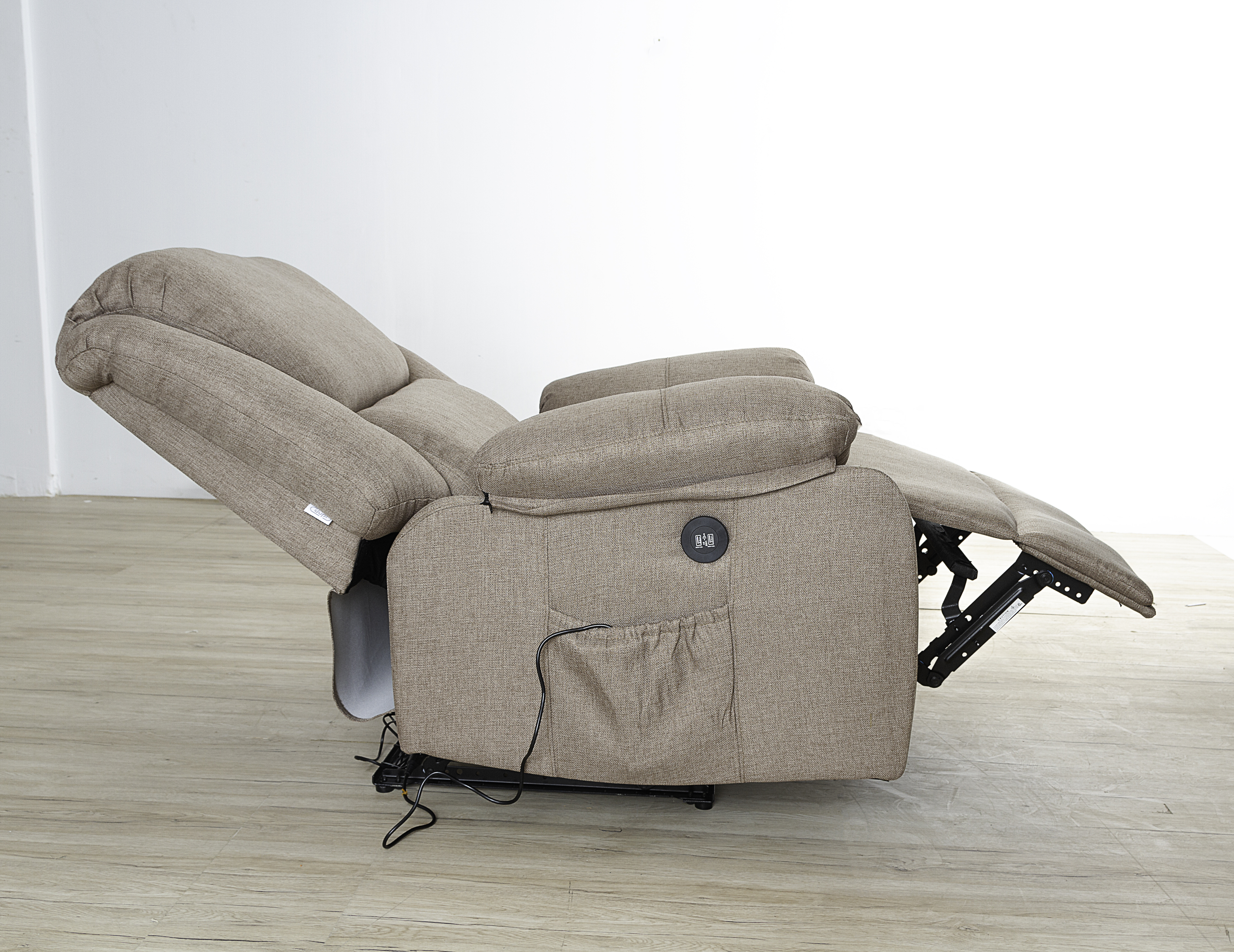 Una silla reclinable beige está parcialmente reclinada sobre un piso de madera, contra una pared blanca.