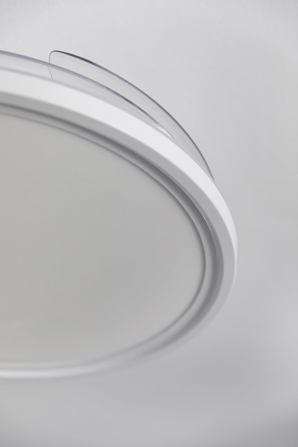 Vista de cerca de una lámpara de techo redonda blanca con una cubierta de plástico transparente y curvada. El fondo es blanco suave.
