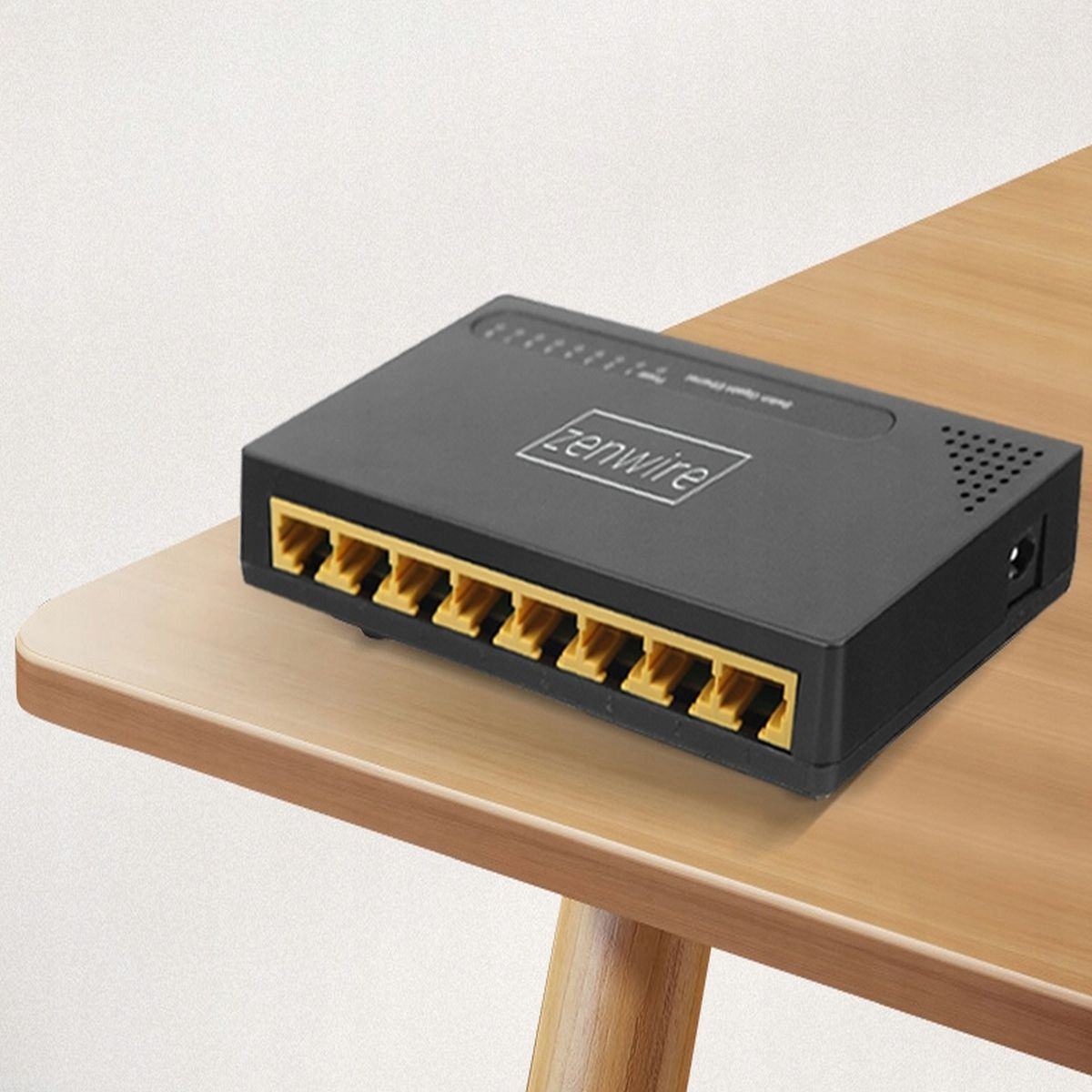Czarny przełącznik sieciowy z żółtymi portami leży na drewnianym stole. Przełącznik ma logo 'zenwire'.