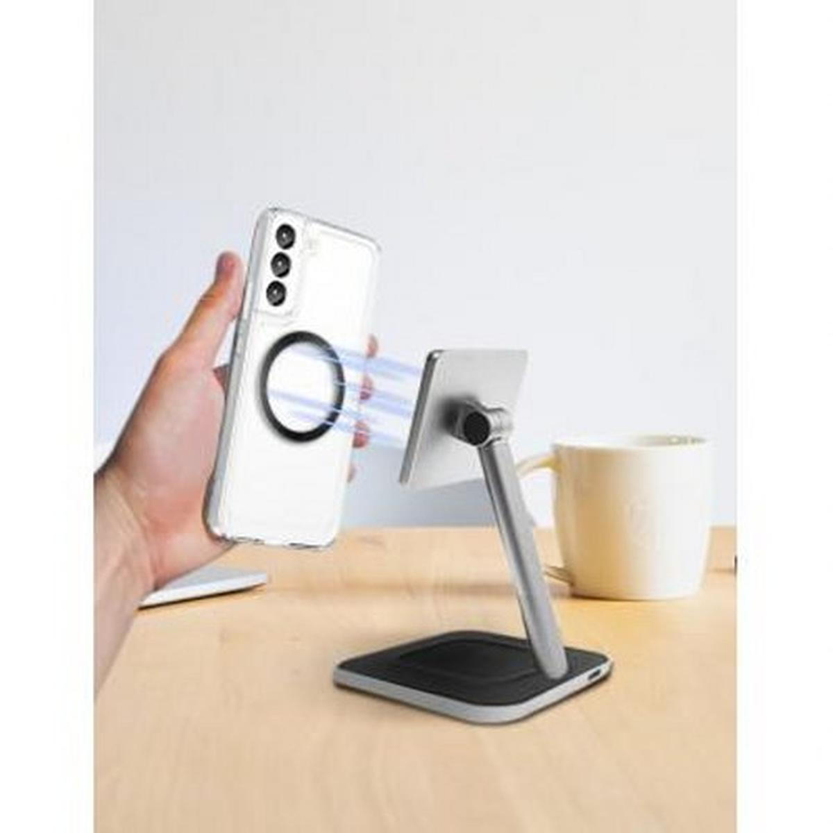 Eine Hand hält ein Telefon in der Nähe eines Telefonständers. Im Hintergrund befindet sich eine Kaffeetasse. Die Handyhülle hat einen schwarzen Ring.