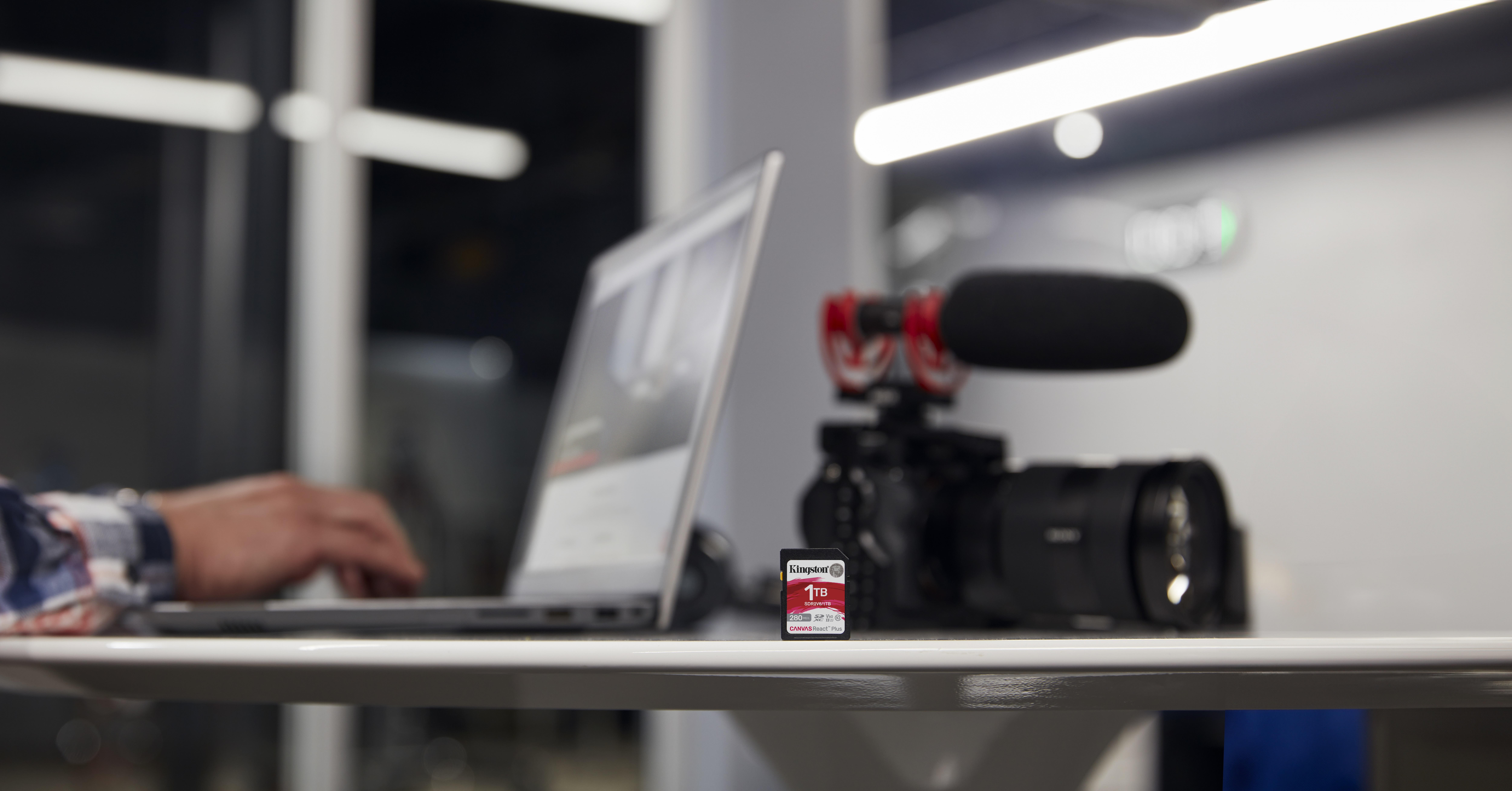 Un ordinateur portable, une caméra et un microphone sont sur un bureau. Une carte SD de 1 To est au premier plan.
