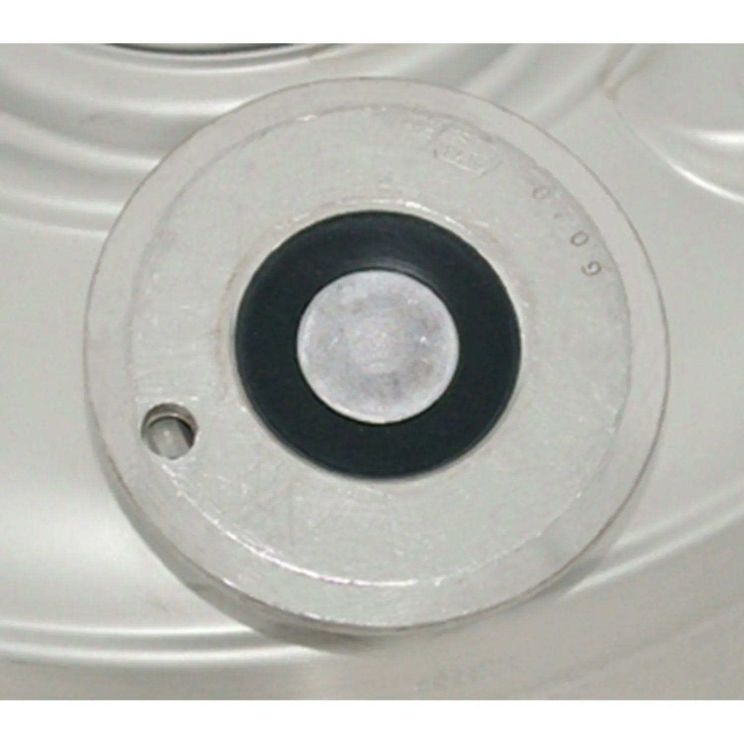 Een metalen schijf met een zwarte rubberen ring rond een kleinere zilveren schijf. De cijfers '6709' zijn zichtbaar.