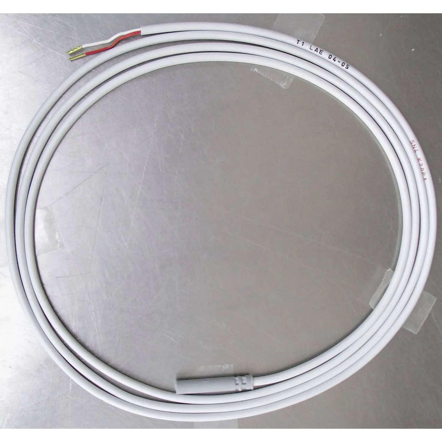 Een witte kabel met draden aan één uiteinde en een grijze connector aan de andere kant. Hij is opgerold op een metalen oppervlak.