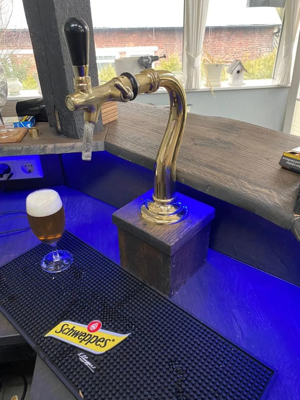 Eine Bar mit Bierhahn, einem Bierglas und einer Schweppes-Matte. Die Bar hat blaue Lichter.