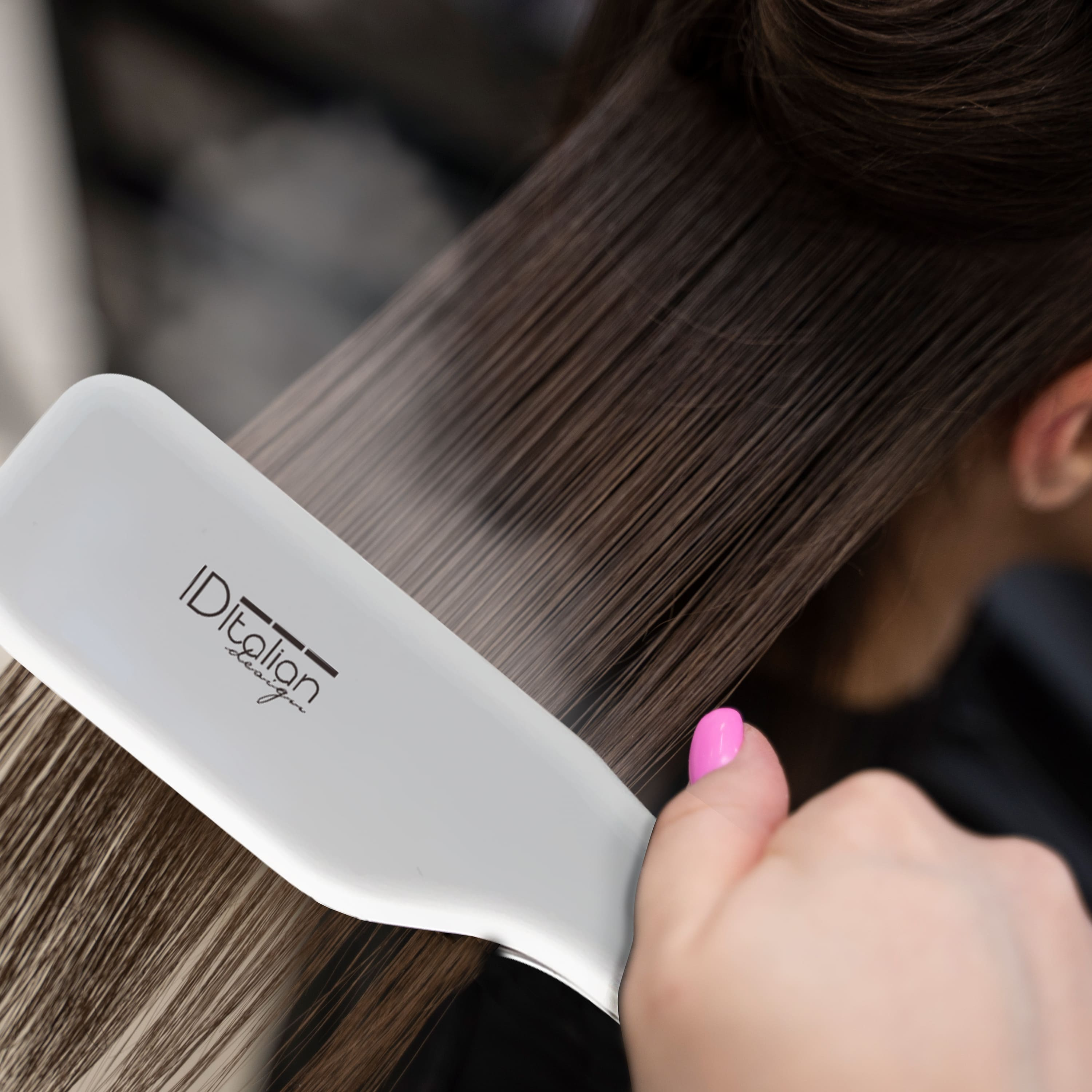 Una piastra bianca con il marchio sta lisciando capelli castani. Una mano con unghie rosa tiene la piastra.