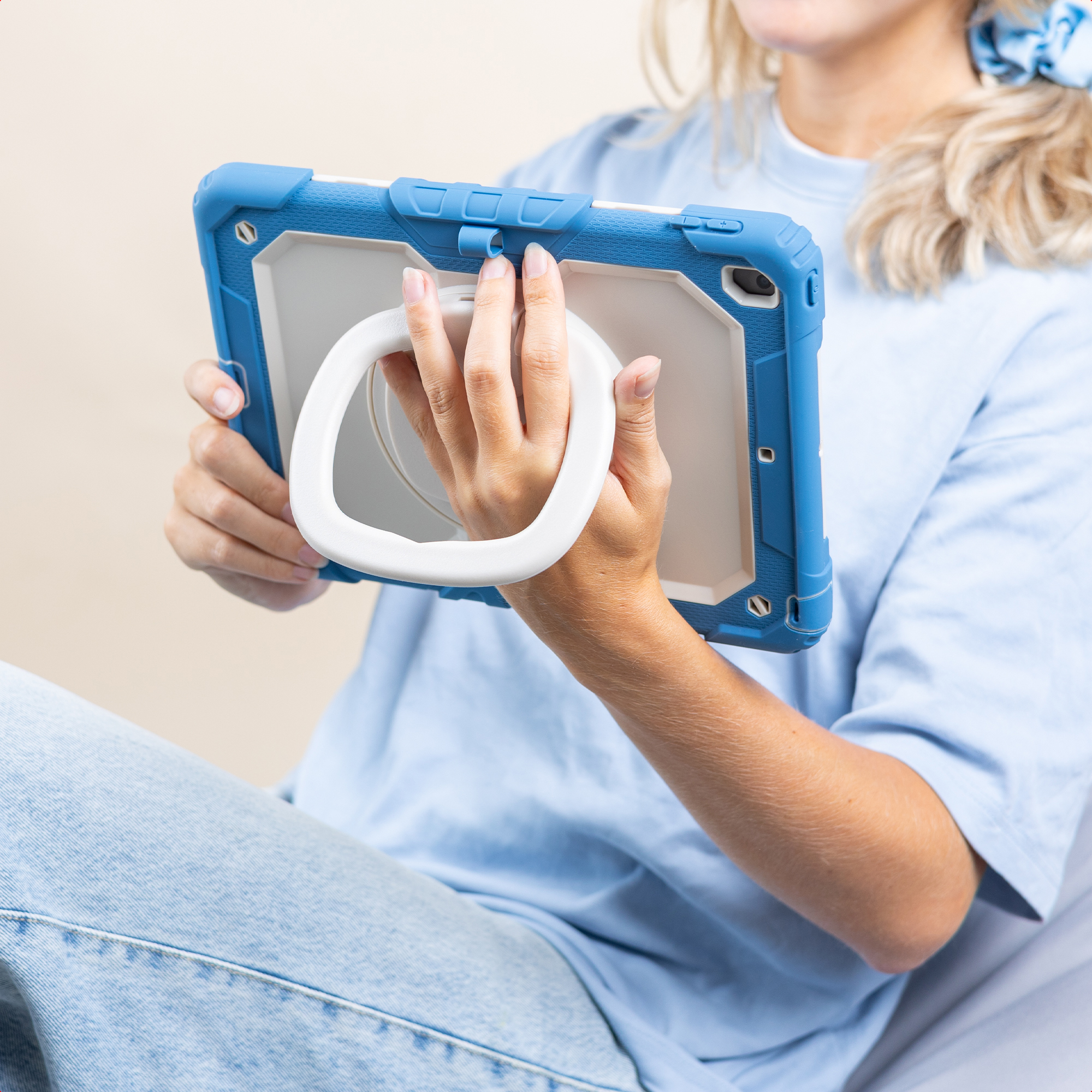 Une personne tient une tablette bleue avec une poignée blanche. Elle porte une chemise bleue et un jean.
