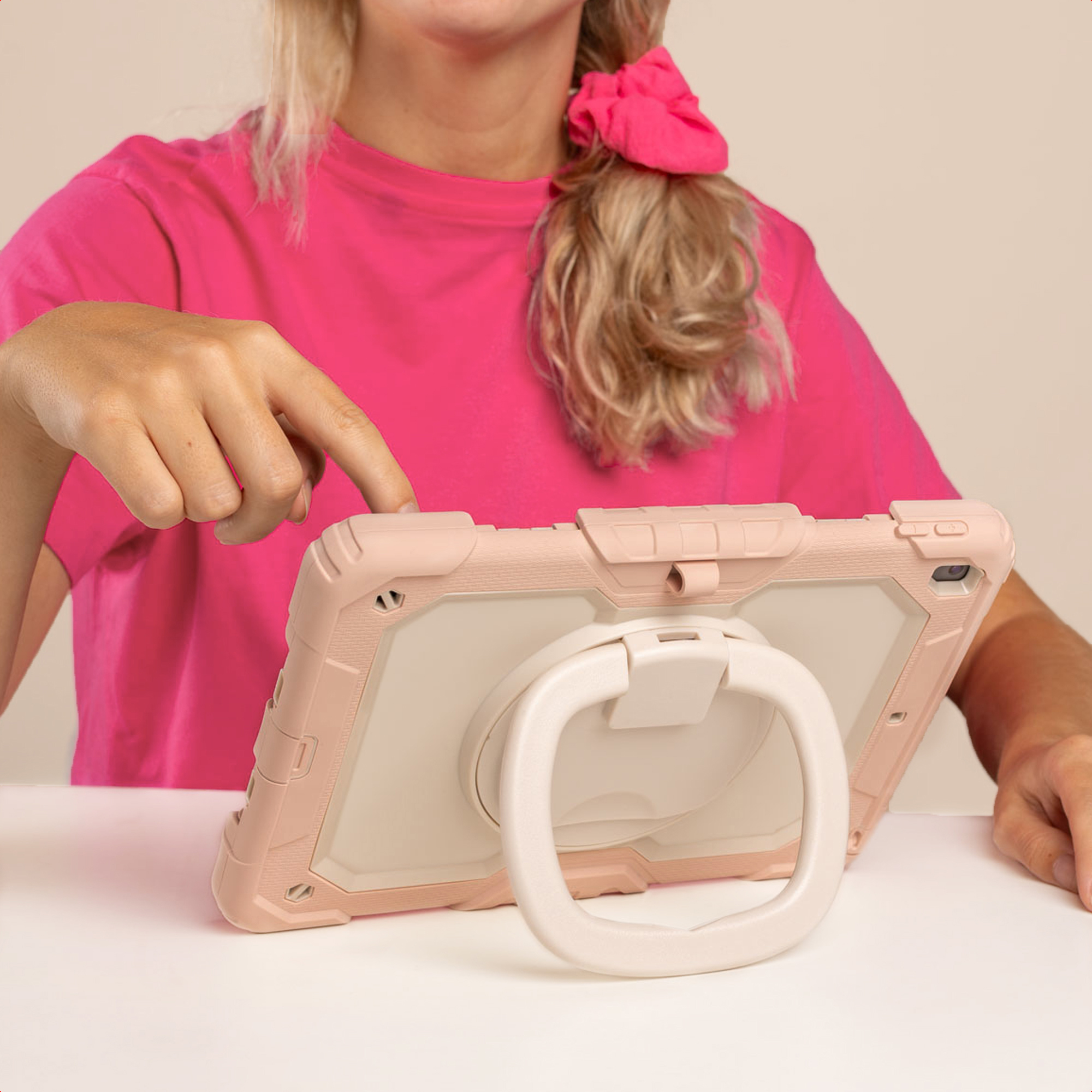 Une personne utilise une tablette. Elle porte des vêtements roses et a les cheveux blonds avec un chouchou rose. La tablette est dans un étui rose.