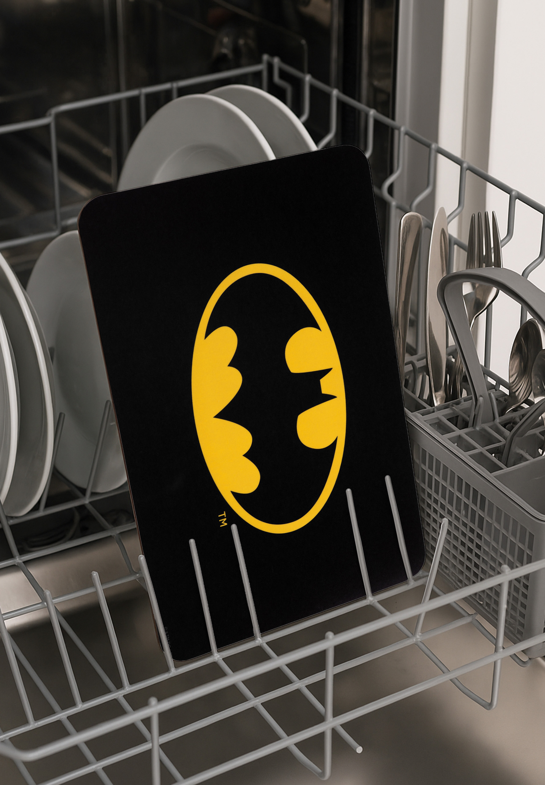 Ein Batman-Logo-Schneidebrett in einer Spülmaschine. Andere Gerichte und Besteck sind sichtbar.