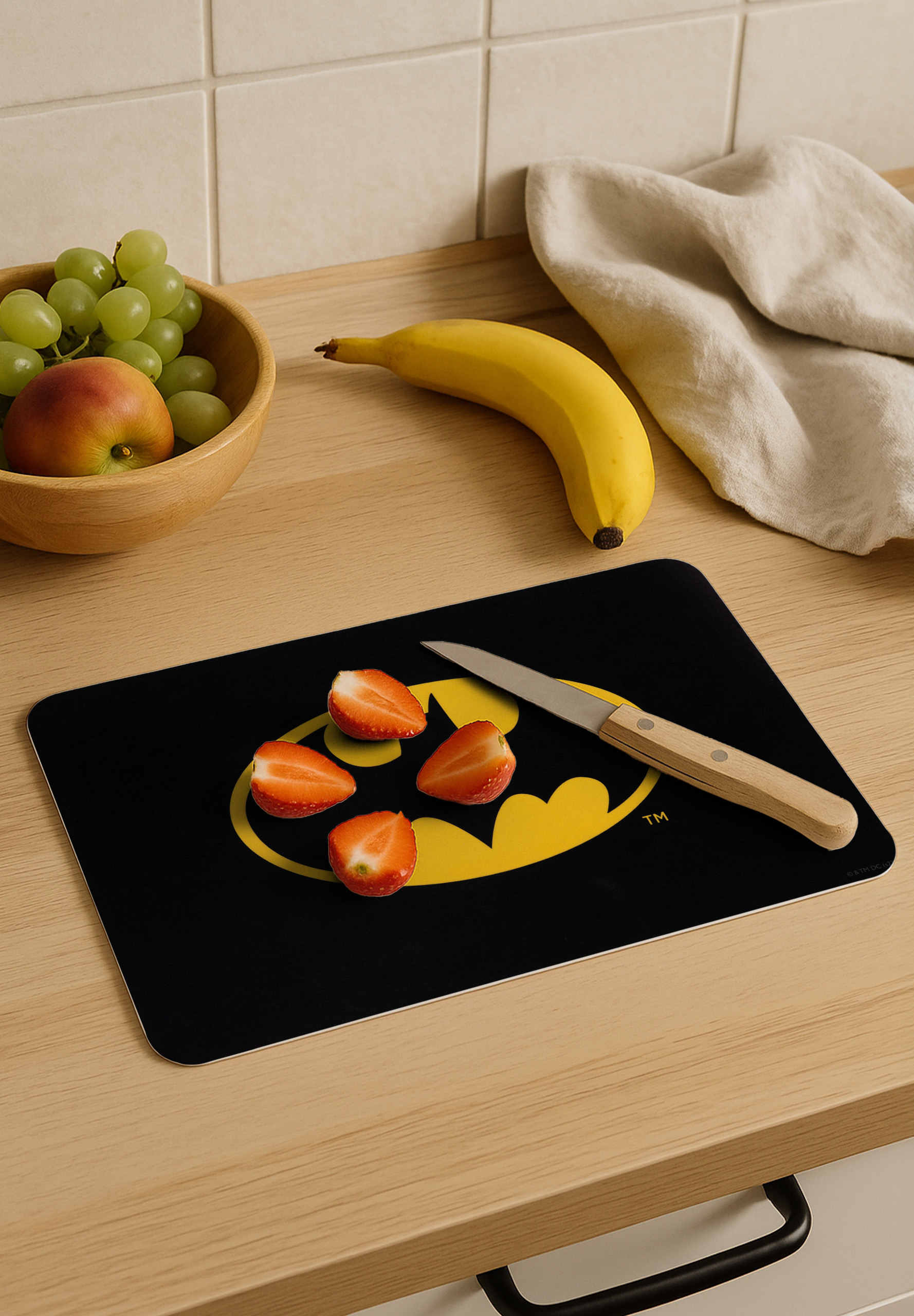 Eine Küchenszene mit Obst, einer Banane und einem Messer auf einem Batman-Schneidebrett.