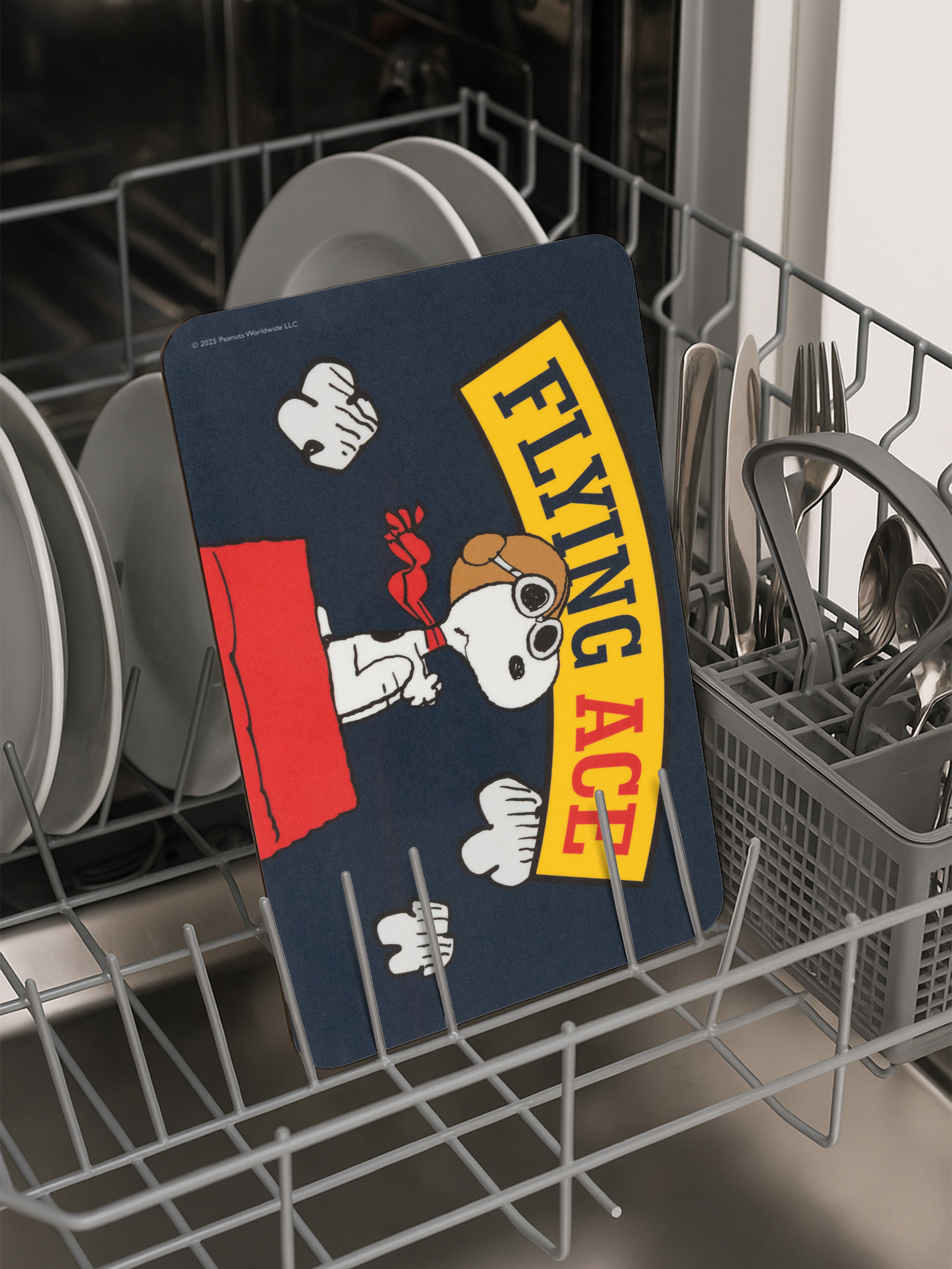 Eine Snoopy Flying Ace-Tischmatte befindet sich in einer Spülmaschine. Teller, Besteck und ein Korb sind ebenfalls sichtbar.