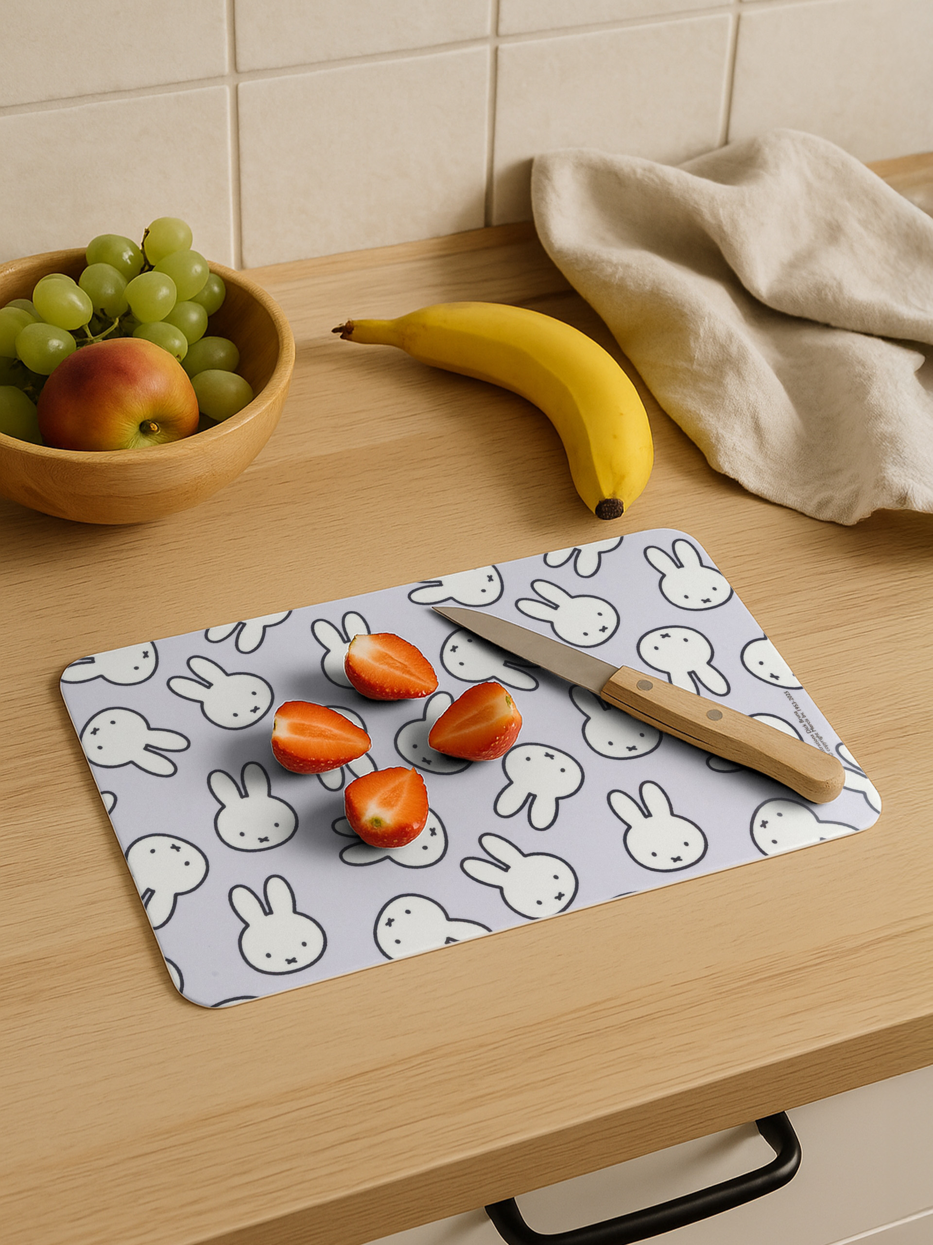 Ein Schneidebrett mit Erdbeeren, einem Messer und einer Banane. Weintrauben und ein Apfel in einer Holzschüssel.