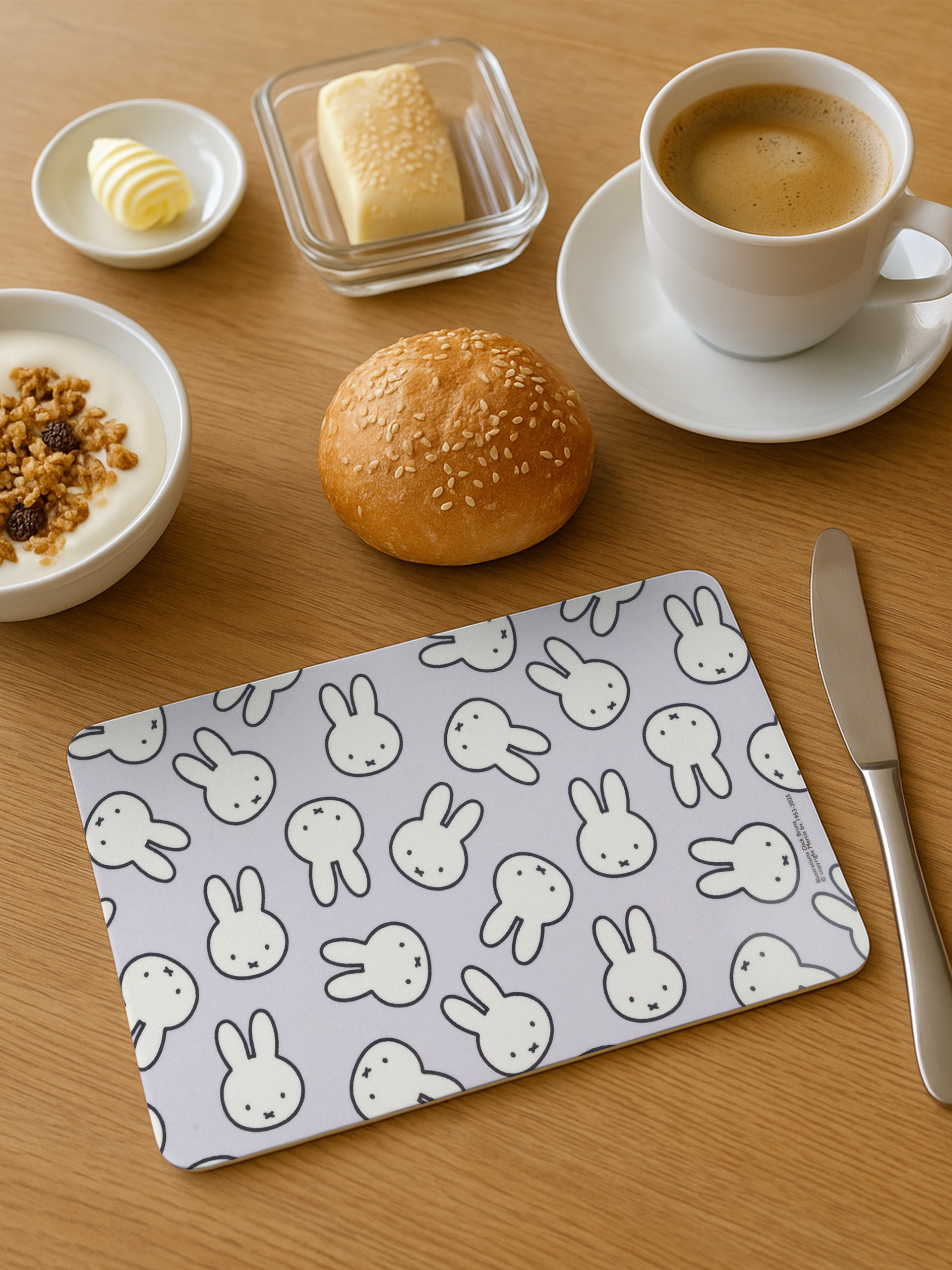 Ein Tisch mit Frühstückszutaten: Kaffee, Butter, Joghurt, Brötchen und eine Matte mit Hasengesichtern. Ein Messer rechts.
