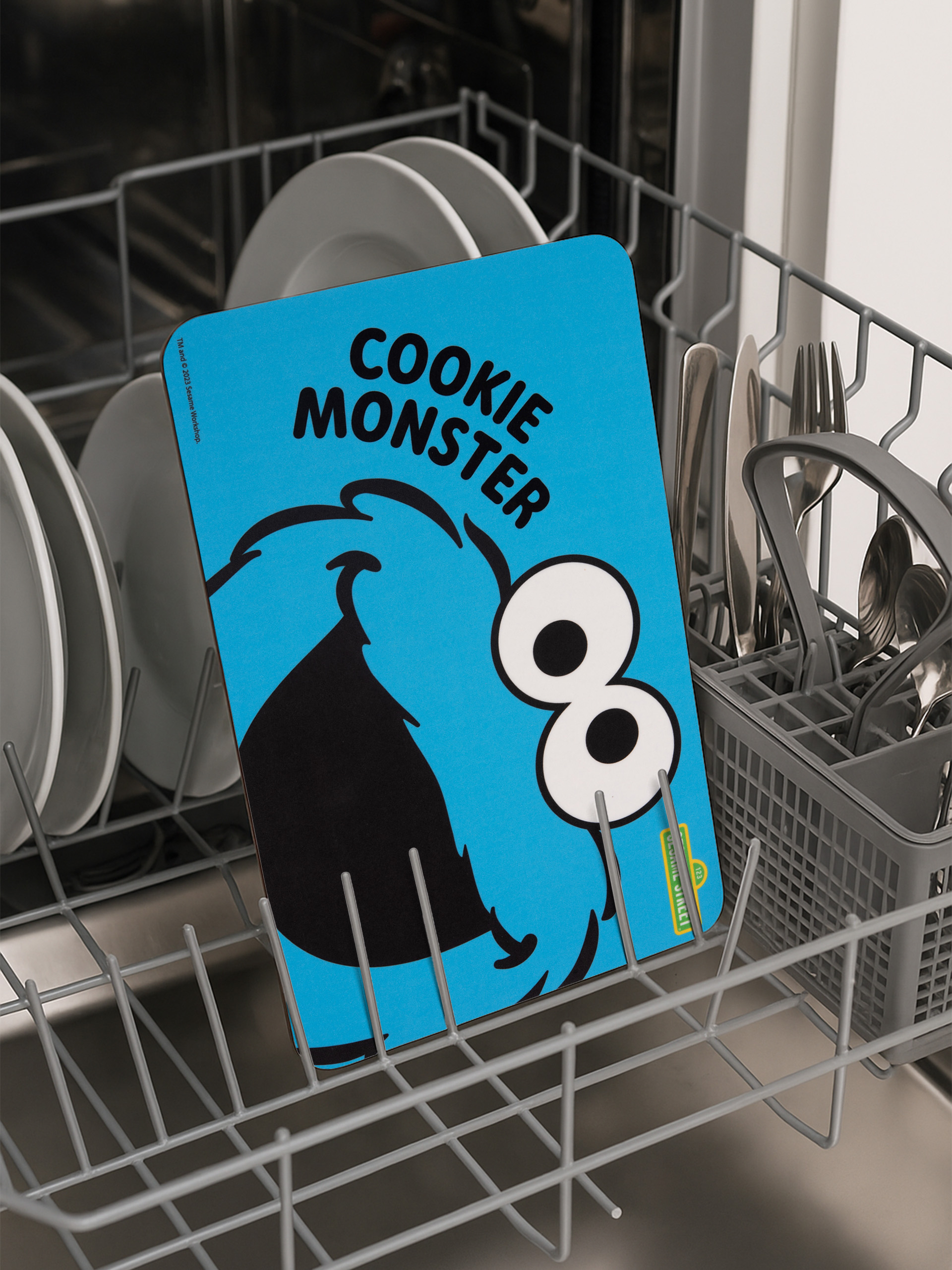Ein Cookie-Monster-Schild befindet sich in einem Geschirrspüler. Geschirr und Besteck sind im Hintergrund.