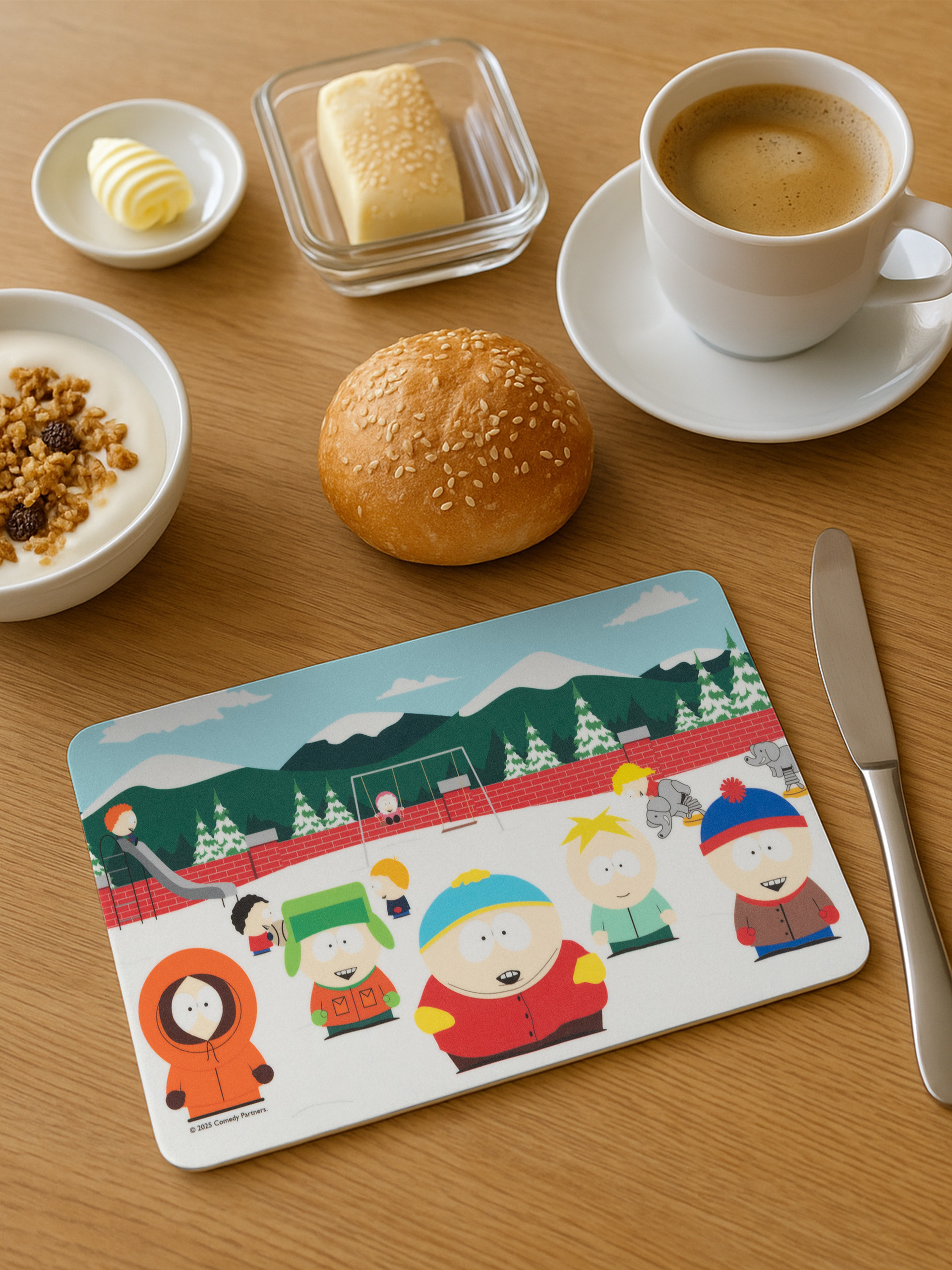 Frühstücksszene mit Kaffee, Joghurt, Butter, Brötchen und einer Tischmatte mit South Park-Charakteren.