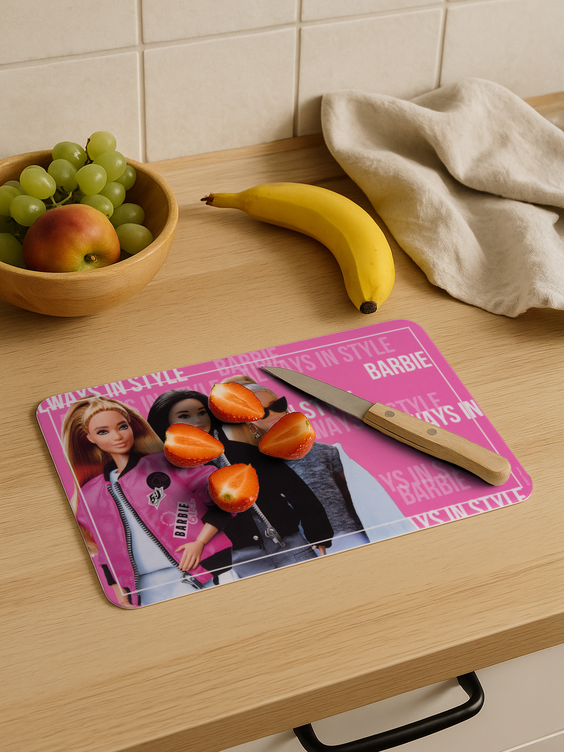 Küchenszene mit Obst, einem Schneidebrett mit Barbie und einem Messer. Erdbeeren sind auf dem Brett geschnitten.