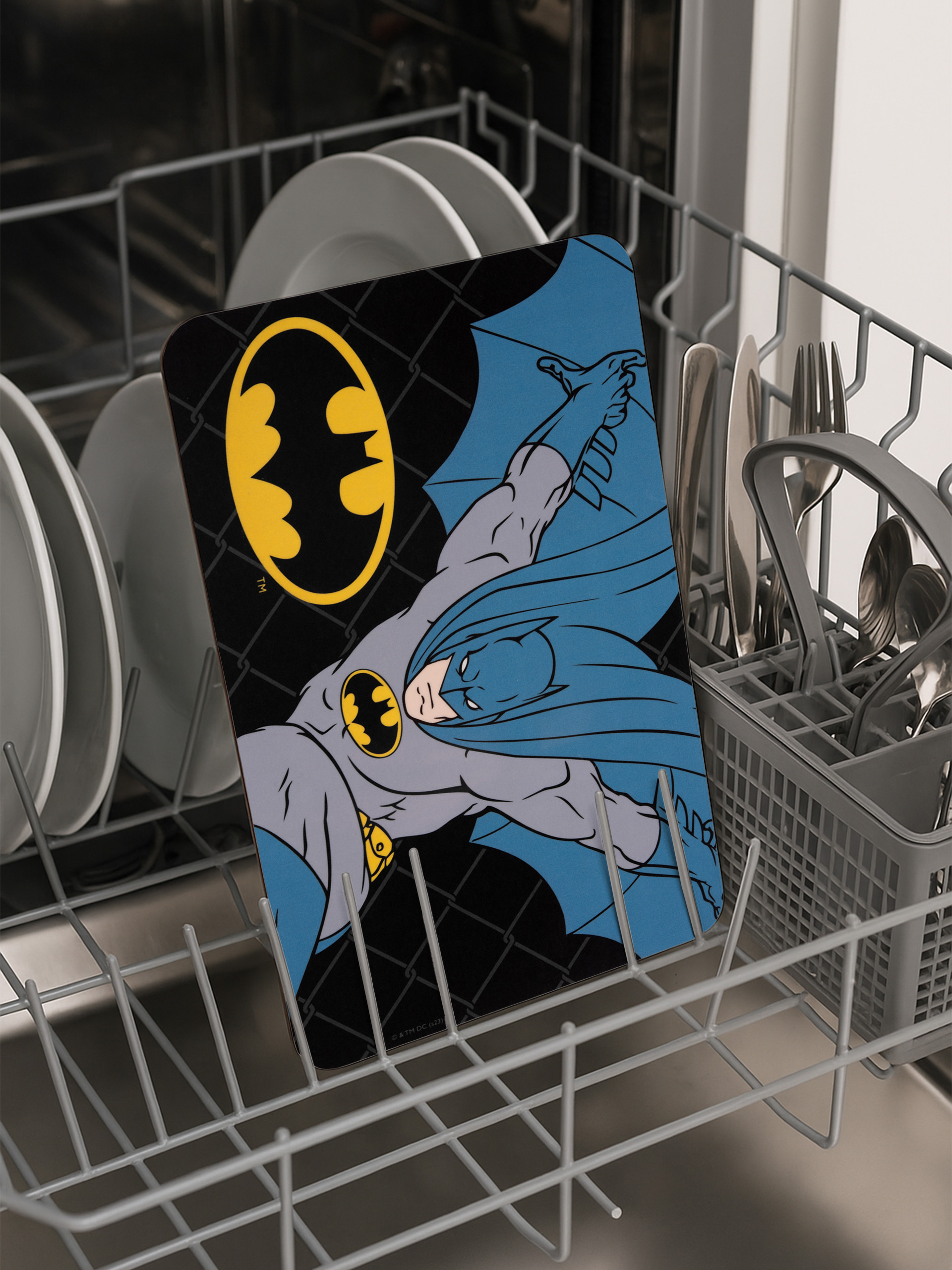Batman-Matte in einer Spülmaschine. Die Matte zeigt Batman. Geschirr und Besteck sind ebenfalls sichtbar.