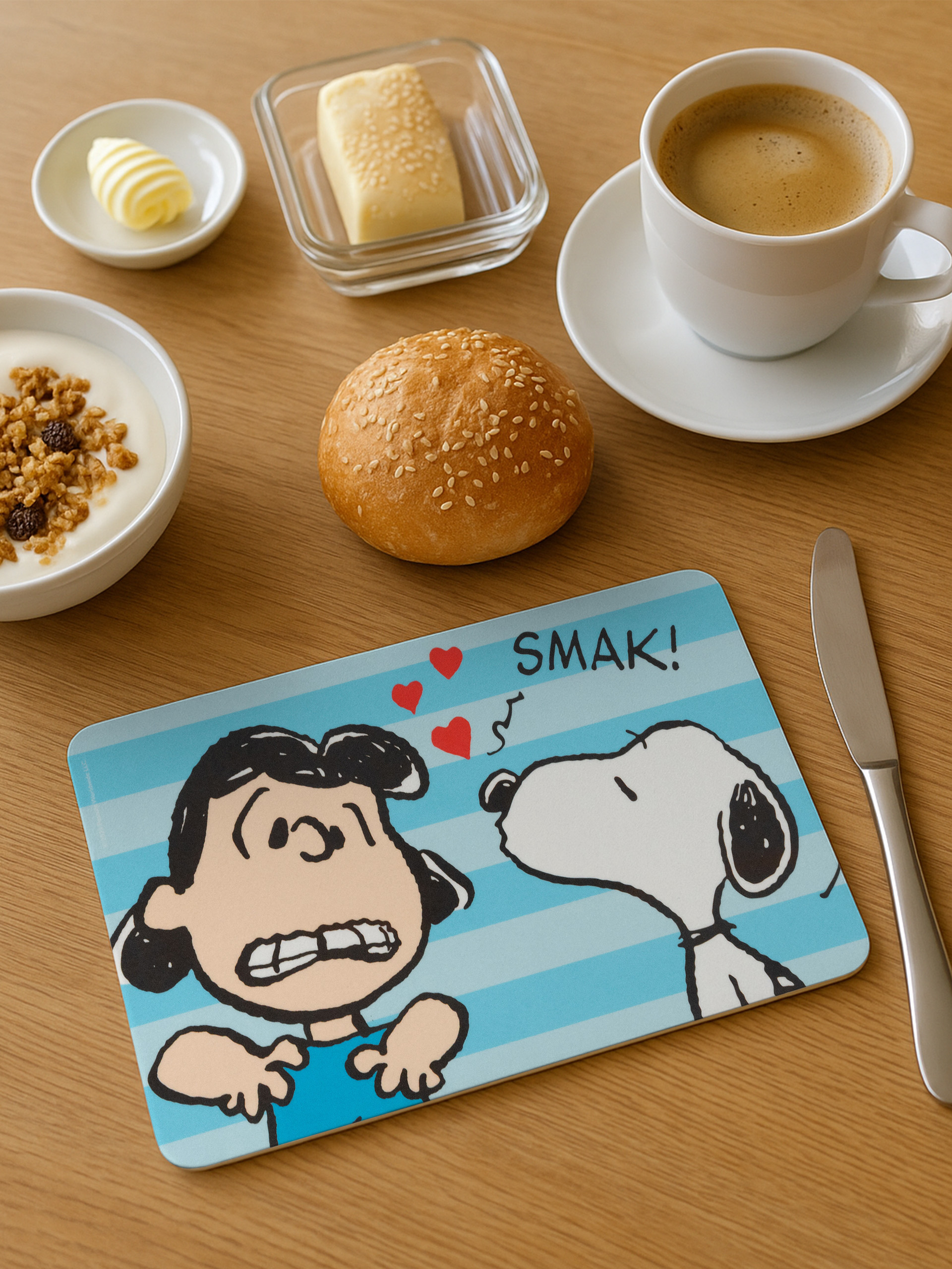 Frühstücksszene: Kaffee, Butter, Joghurt, Brot und eine Snoopy-Tischmatte. Ein Messer ist rechts.