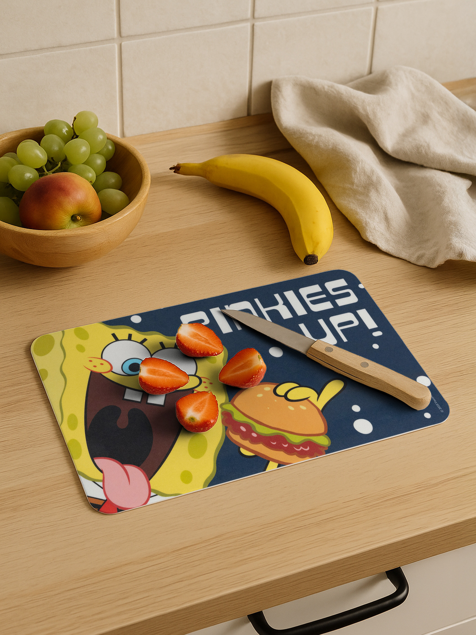 Küchenszene mit SpongeBob-Schneidebrett, Erdbeeren, Banane, Trauben und einem Messer.