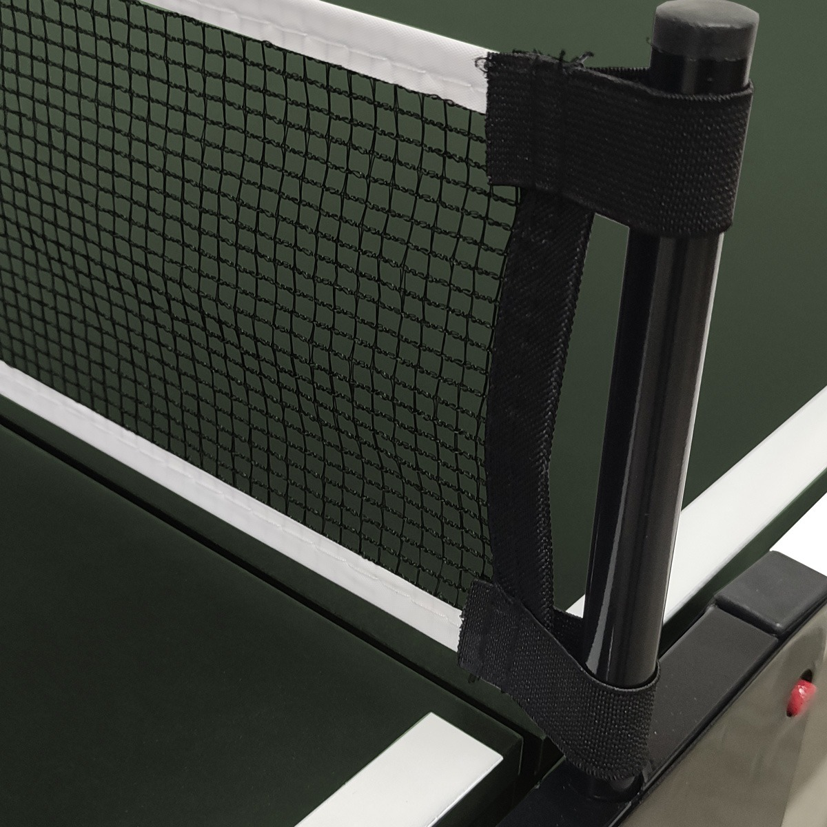 Close-up of a ping pong table net. The net is black and white, supported by a black pole. The table is green.