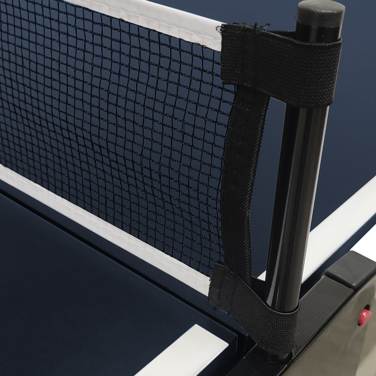 A close-up view of a ping pong net. The net is black, and the table is blue. A black pole supports the net.