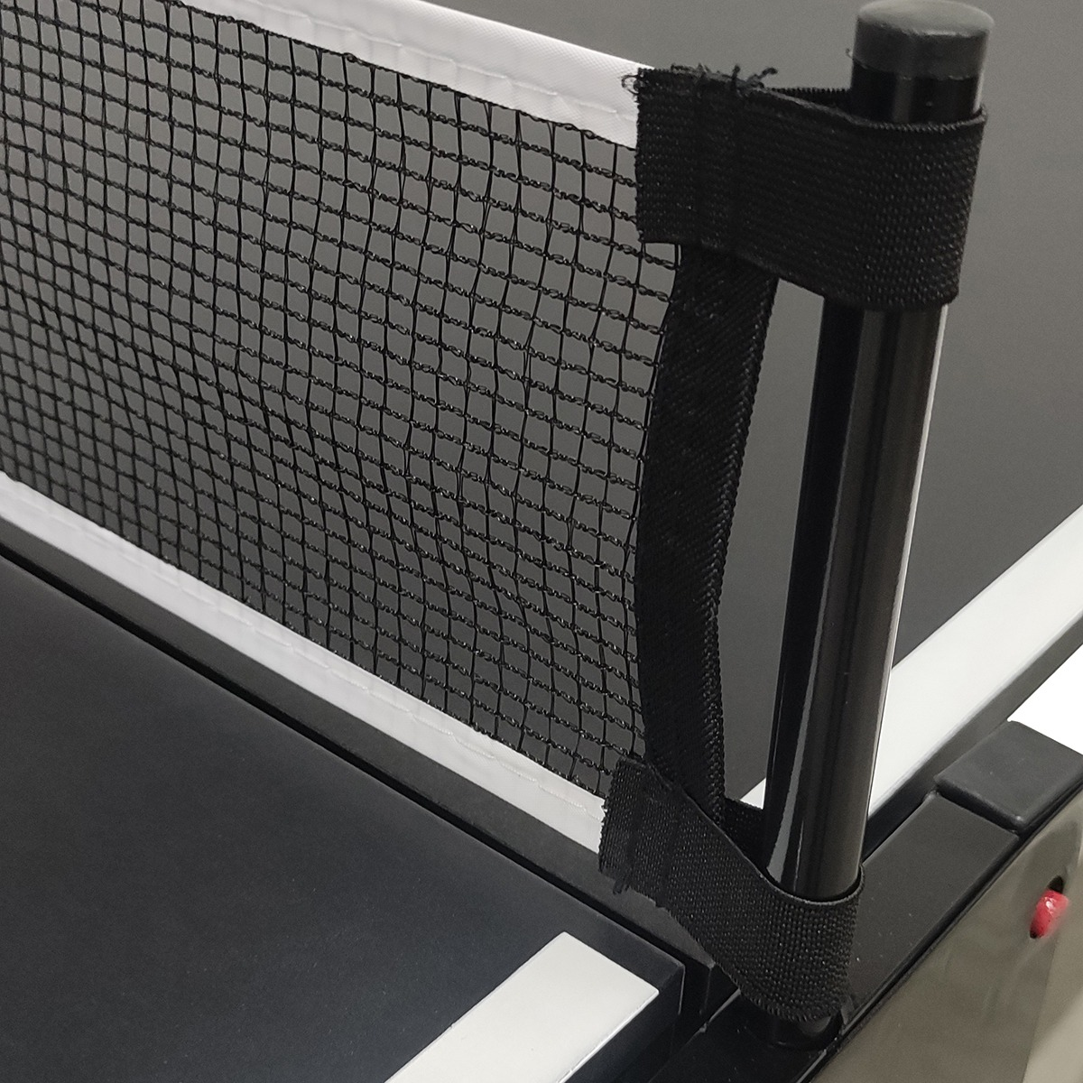 A close-up of a table tennis net. The net is black, and attached to a black pole. The table is black with white lines.