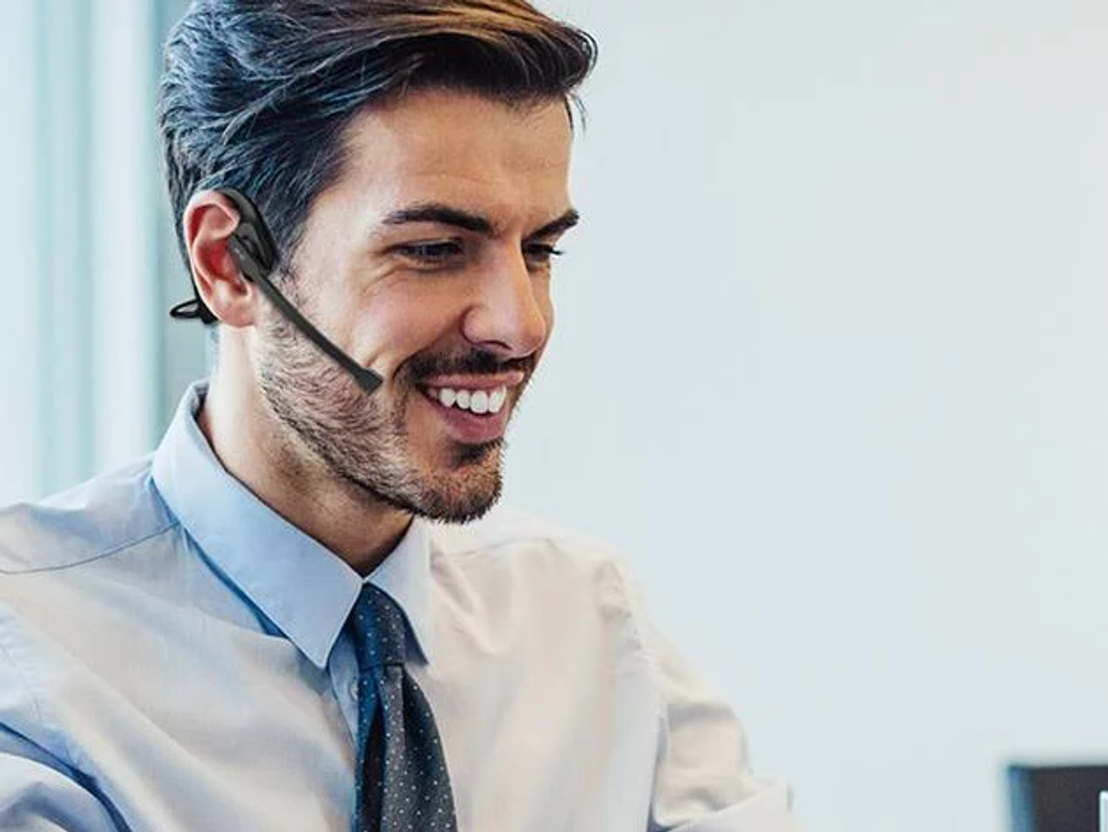 Un uomo sorridente con un auricolare. Indossa una camicia blu e una cravatta. Lo sfondo è sfocato.