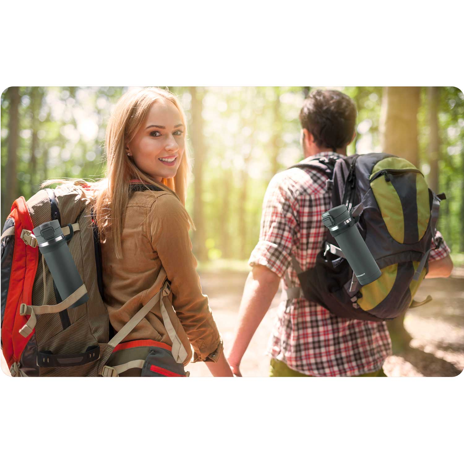 Para wędruje po lesie, trzymając się za ręce. Mają plecaki z butelkami wody. Kobieta patrzy w kamerę i się uśmiecha.
