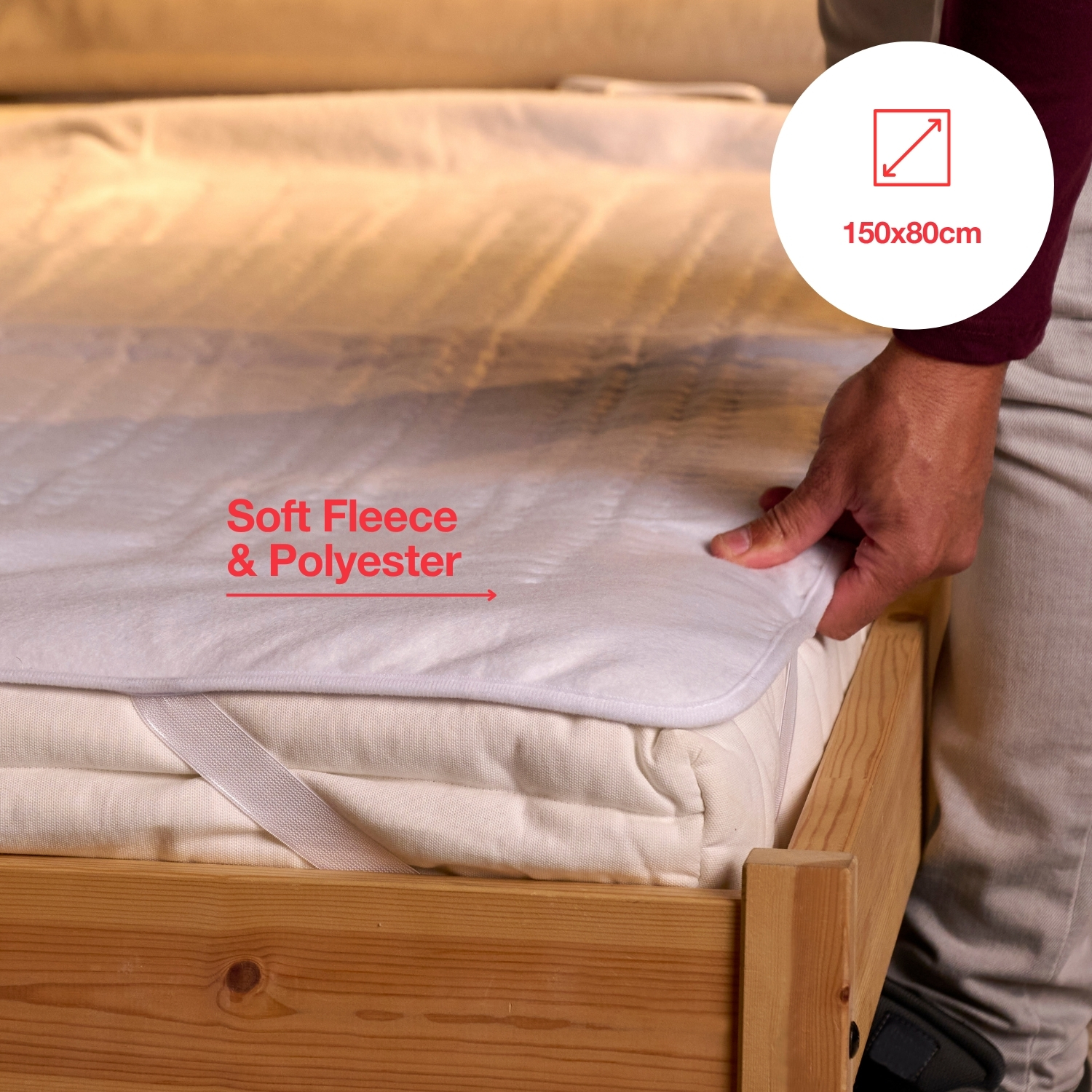 Osoba umieszcza białą osłonę materaca na łóżku. Pokrywa jest oznaczona 'Soft Fleece & Polyester'. Etykieta rozmiaru pokazuje 150x80cm.