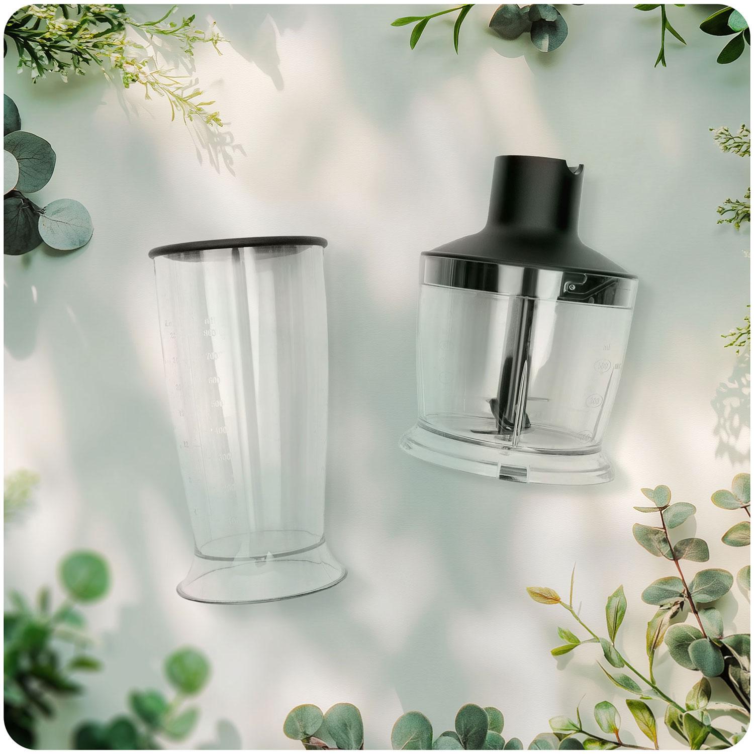 Dwie przezroczyste plastikowe części blendera na białej powierzchni, otoczone zielonymi liśćmi. Jedna część to pojemnik, druga to silnik.