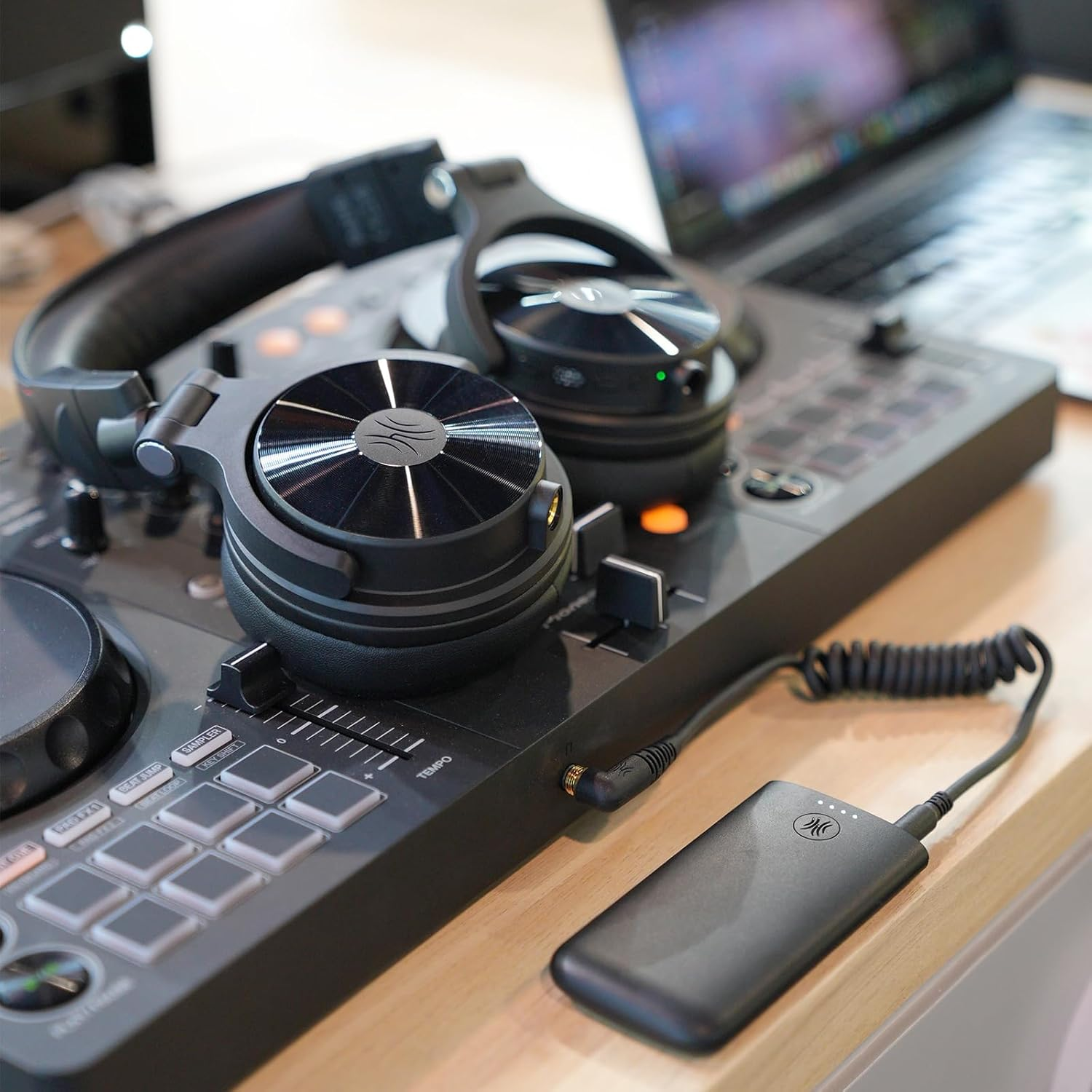 DJ-opstelling met koptelefoon op een mixer, aangesloten op een powerbank. Een laptop op de achtergrond.