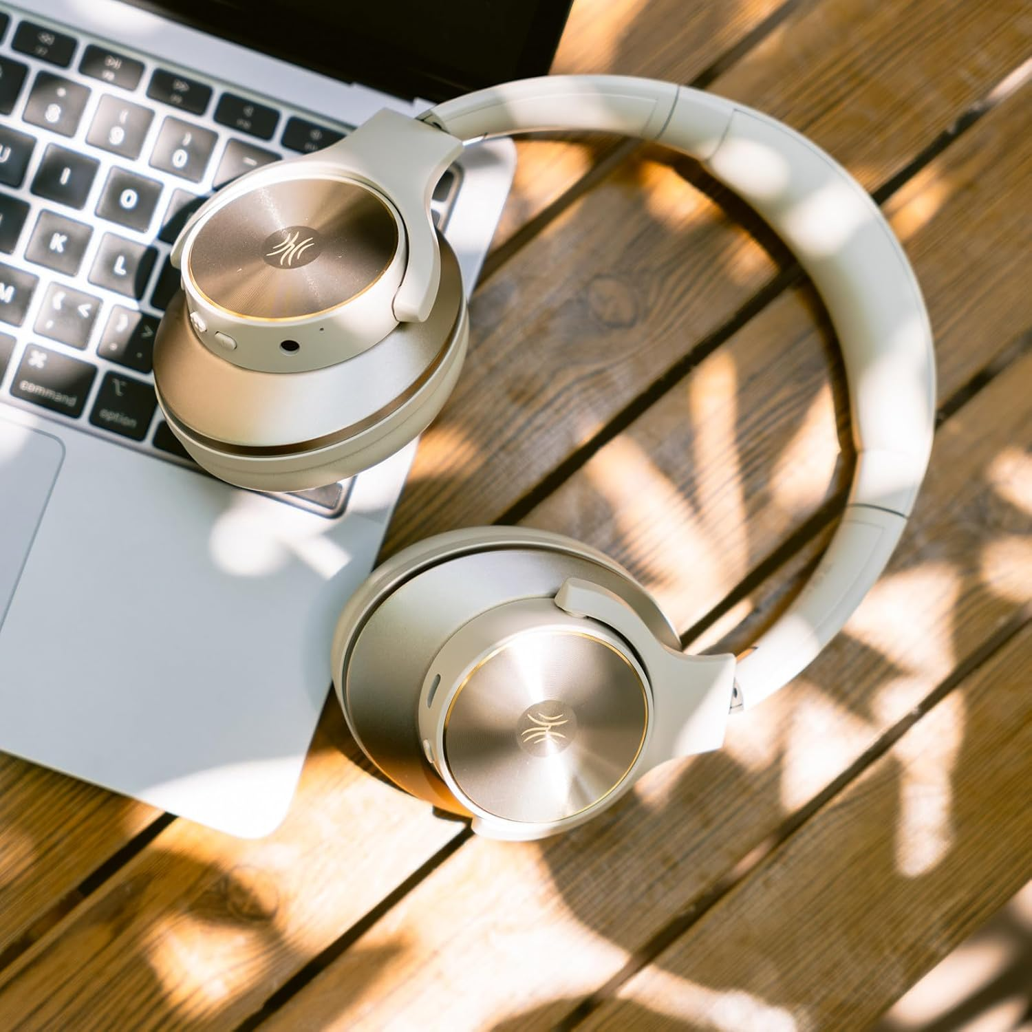 Over-Ear-Kopfhörer auf einer Laptop-Tastatur und einem Holztisch. Die Kopfhörer sind gold und weiß. Der Tisch hat Schatten.