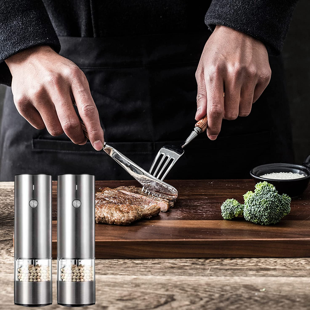 Eine Person schneidet ein Steak mit Gabel und Messer auf einem Holzbrett. Zwei Pfeffermühlen sind im Vordergrund.