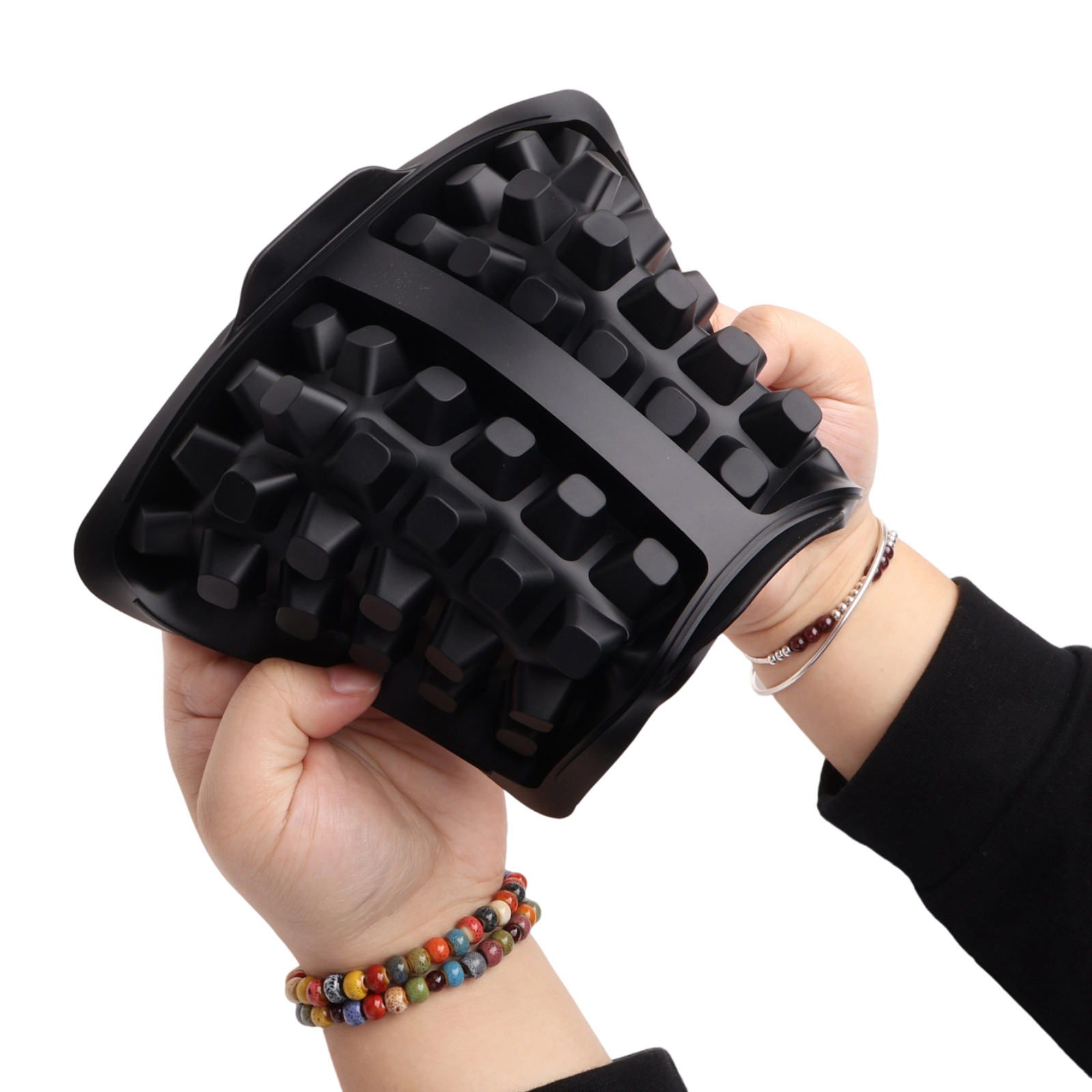 Hände halten ein schwarzes, strukturiertes Objekt. Die Hände tragen Armbänder und ein silbernes Armband. Weißer Hintergrund.