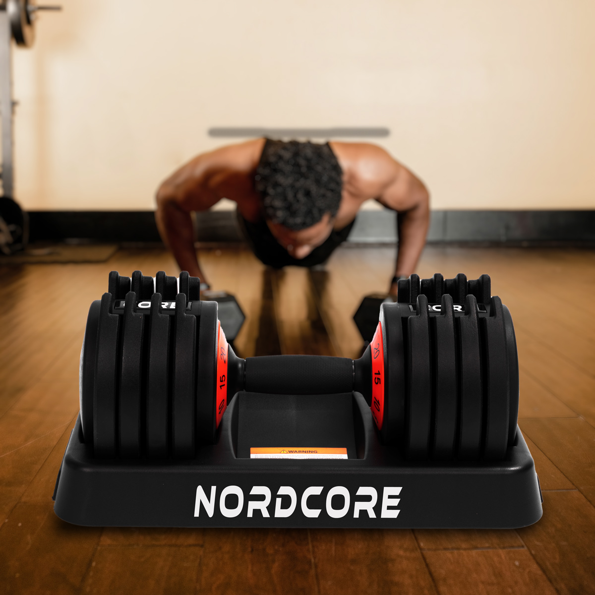 Ein Mann macht Liegestütze in einem Fitnessstudio. Eine Hantel befindet sich im Vordergrund. Das Wort NORDCORE steht auf der Basis der Hantel.