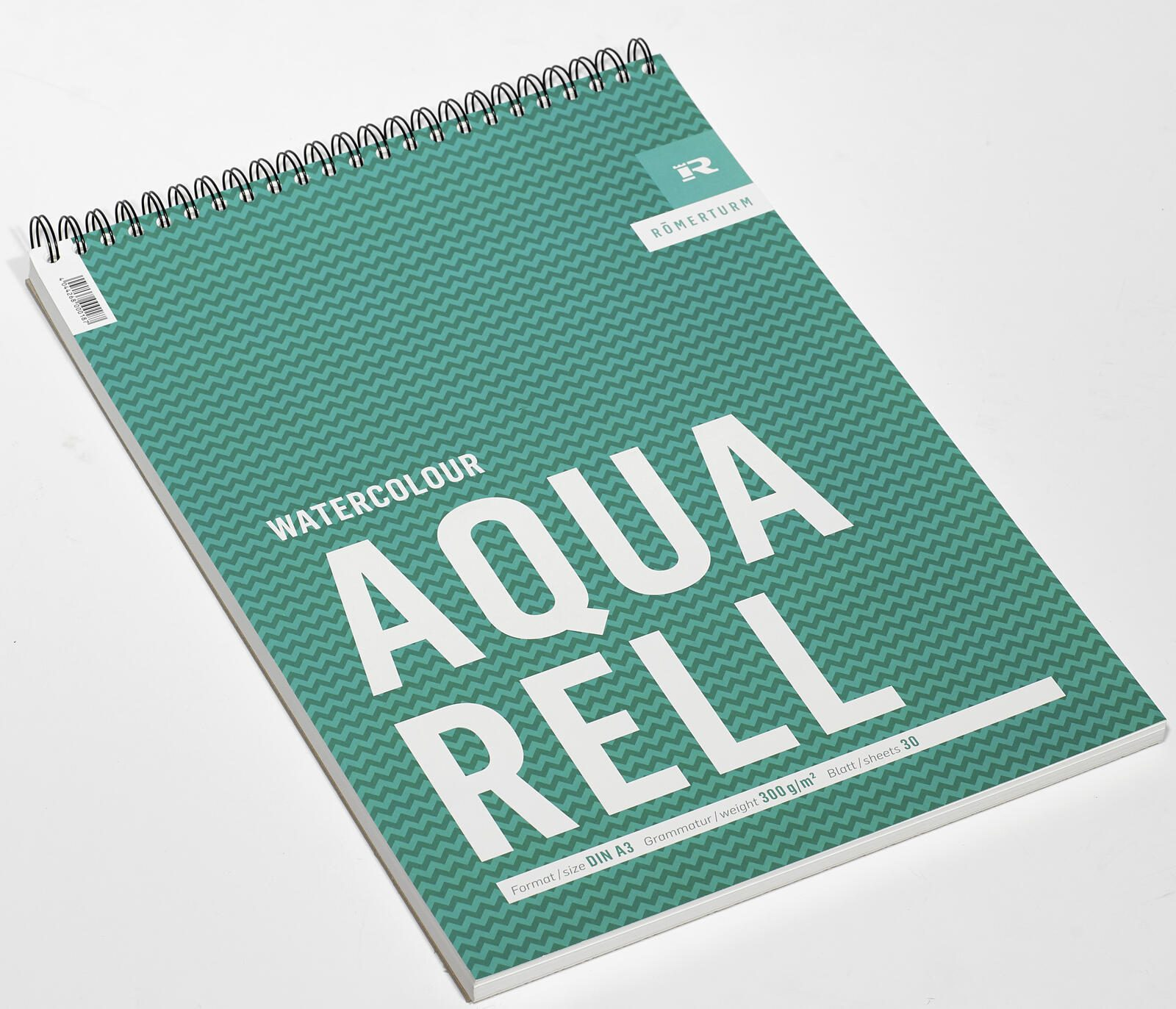 Aquarellblock auf Weiß. Grün gemusterter Einband mit weißem Text. Oben spiralförmig gebunden. Der Block trägt den Titel 'AQUA RELL'.