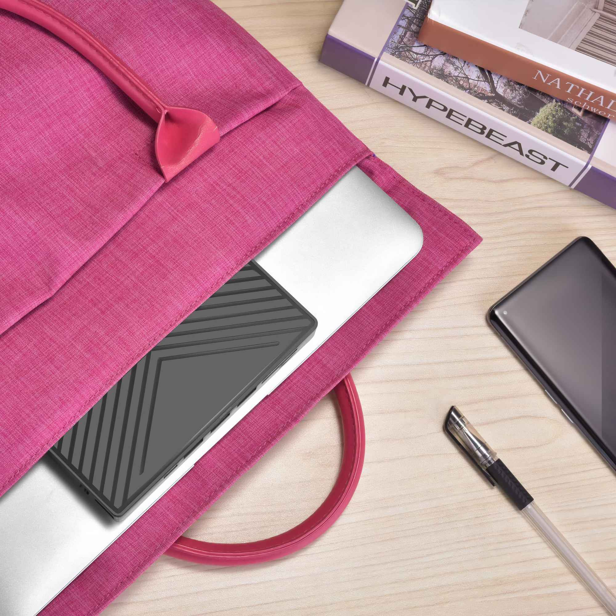 Eine pinkfarbene Laptoptasche mit einem Laptop darin. Auf der Holzoberfläche liegen ein Telefon, ein Stift und ein Buch.