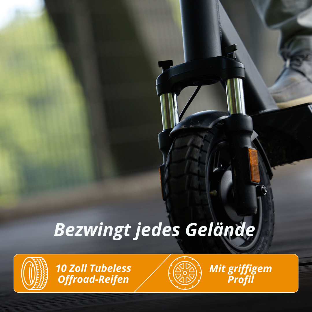 Nahaufnahme des Vorderrads eines schwarzen Elektrorollers mit Offroad-Reifen. Fuß sichtbar. Text: Bezwingt jedes Gelände.