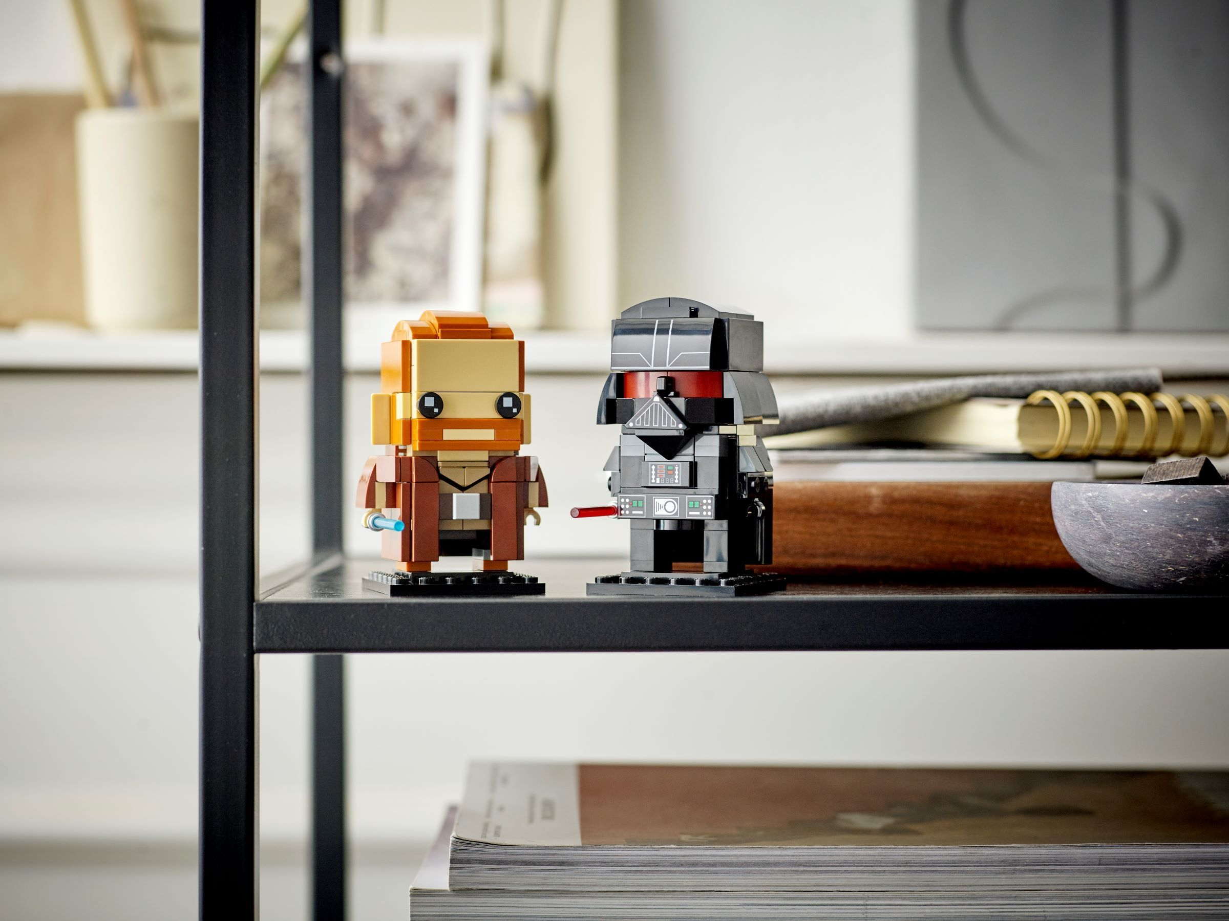 Zwei Lego Star Wars Figuren auf einem Regal: Obi-Wan Kenobi und Darth Vader. Bücher und Dekorationsartikel im Hintergrund.