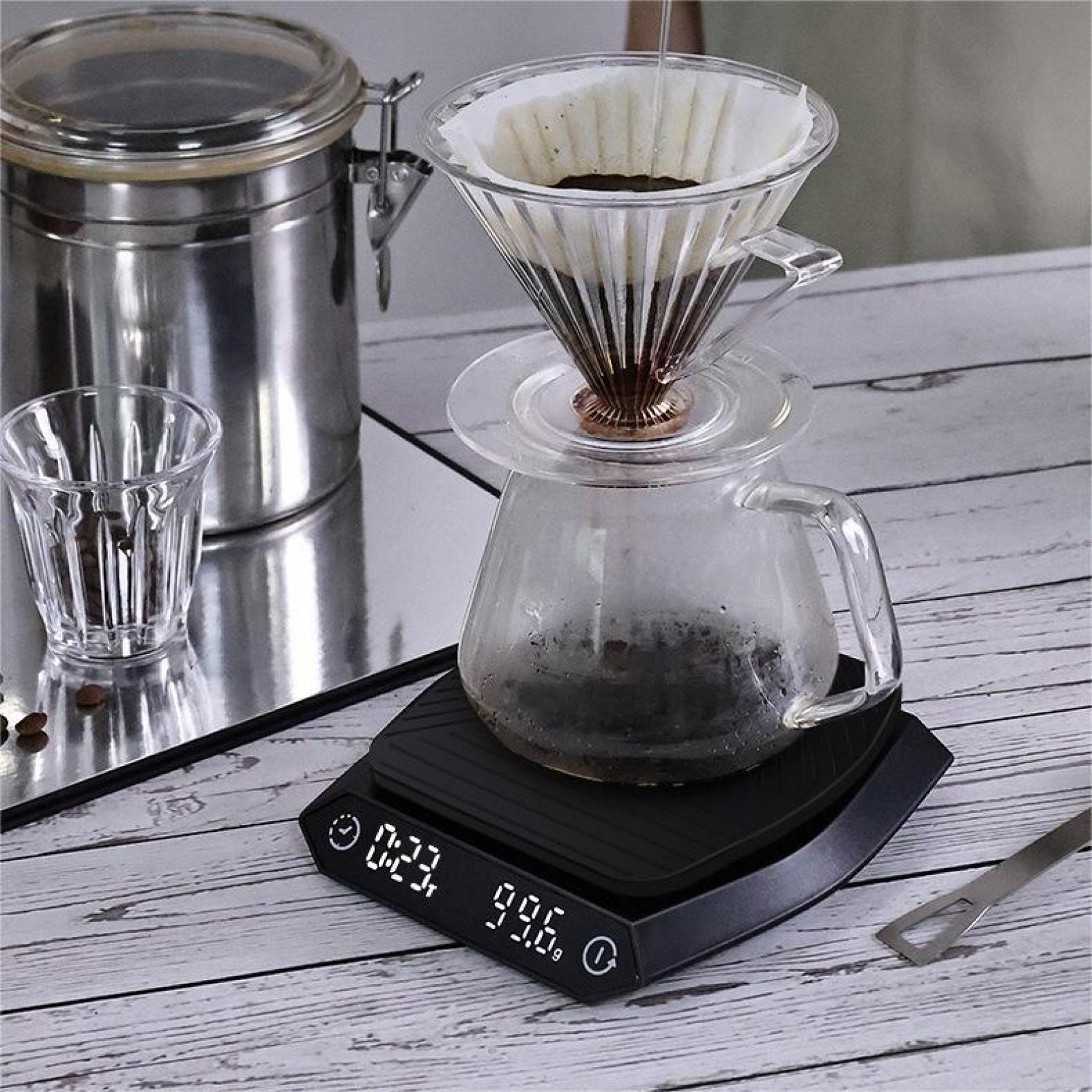 Ein Kaffee-Setup mit Glaskaraffe, Filter, Waage und Glas auf Holz. Wasser gießt.
