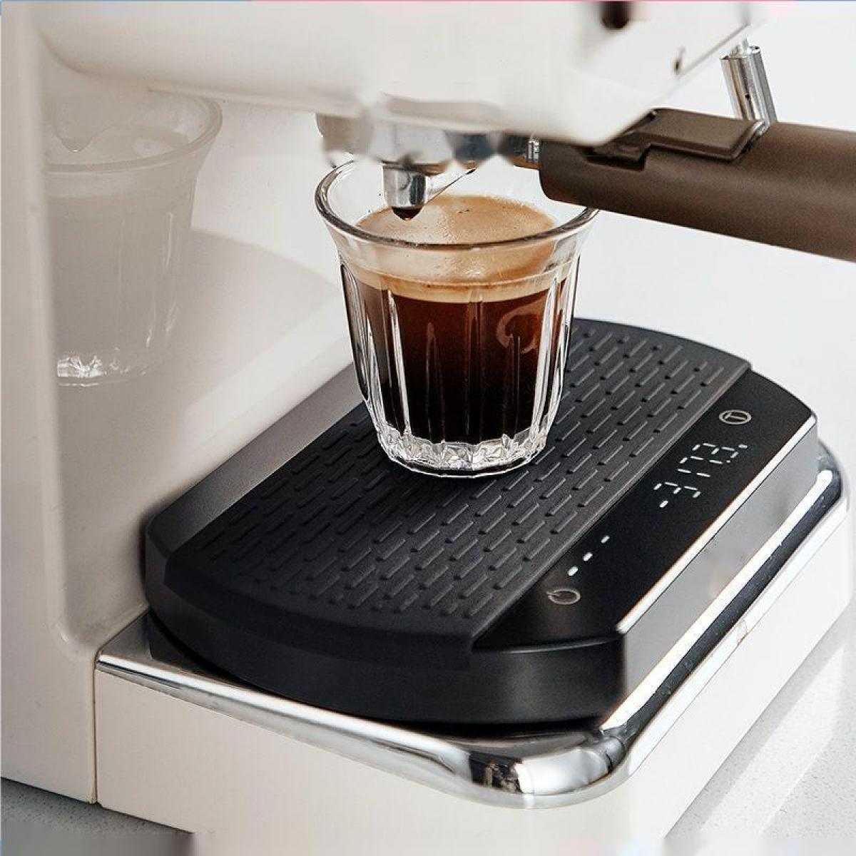Ein Glas Espresso auf einer schwarzen Waage unter einer Espressomaschine. Der Espresso ist dunkel mit Crema.