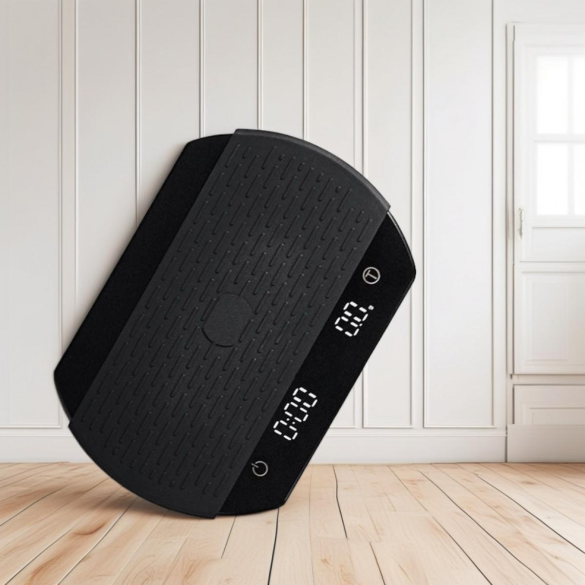 Ein schwarzes Fitness-Balance-Board mit Digitalanzeige, das an einer weißen Wand und einem Holzboden lehnt. Im Hintergrund ist ein Fenster.