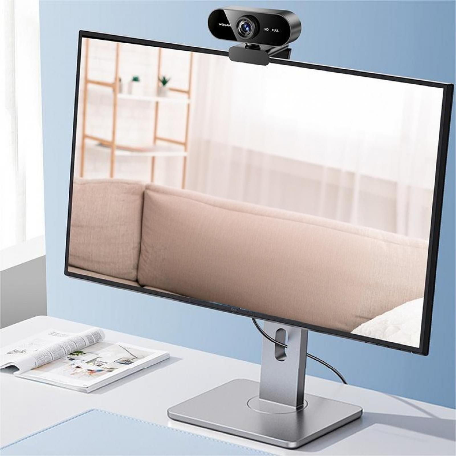 Eine Webcam sitzt auf einem Monitor, der einen Raum mit Sofa reflektiert. Ein Magazin und ein Mauspad liegen auf dem Schreibtisch.
