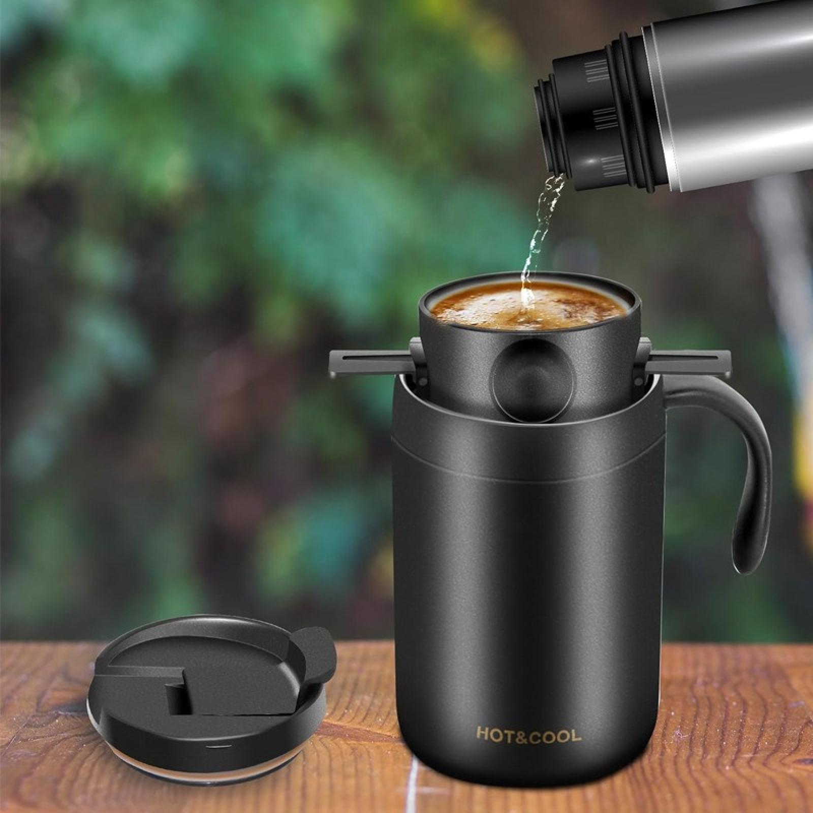 Kaffee wird in einen schwarzen Becher gegossen, mit einem Deckel daneben. Der Hintergrund ist verschwommenes grünes Laub.