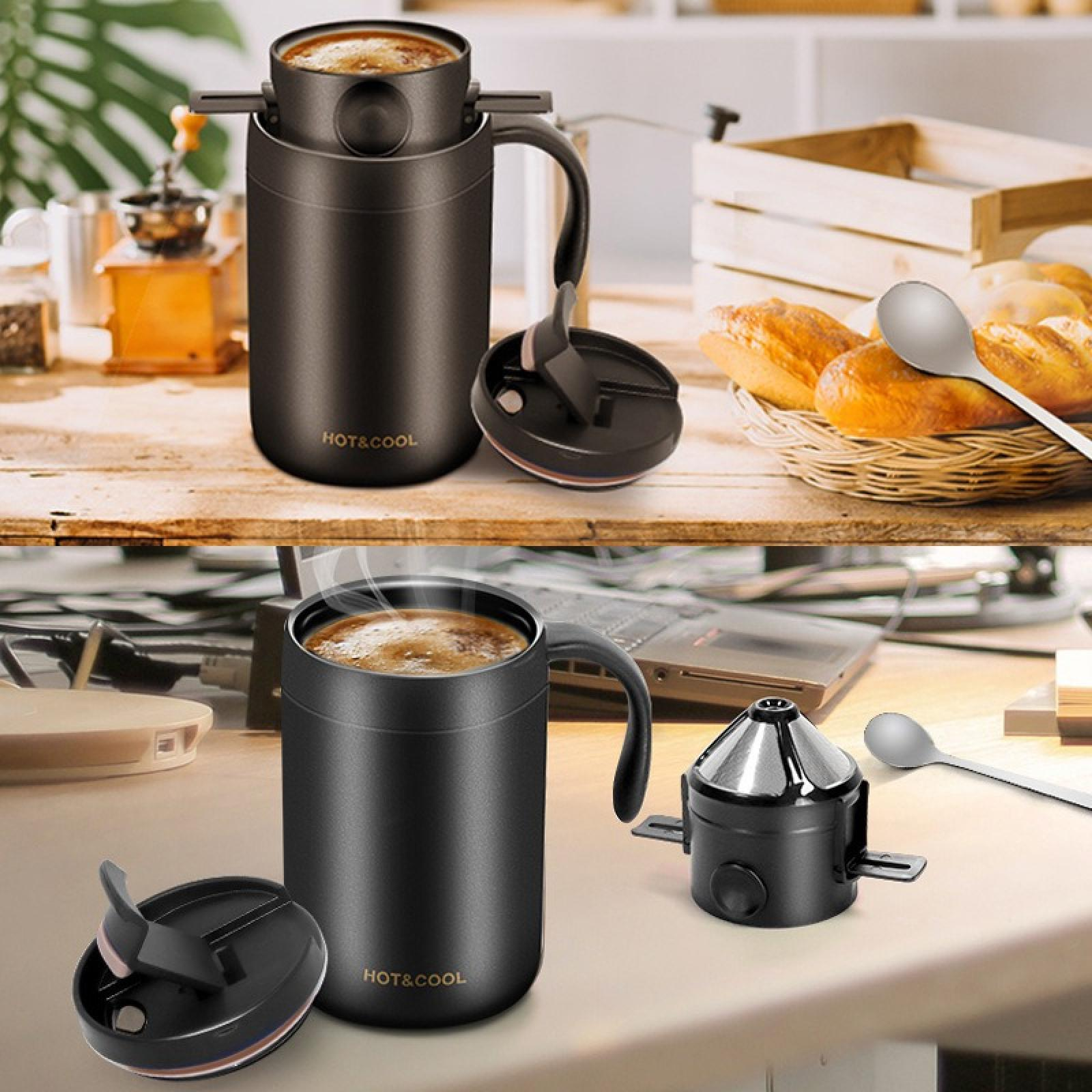 Schwarze Kaffeetassen mit Deckeln, eine kleine Kaffeemaschine, Löffel, Brot und ein Laptop auf einem Holztisch.