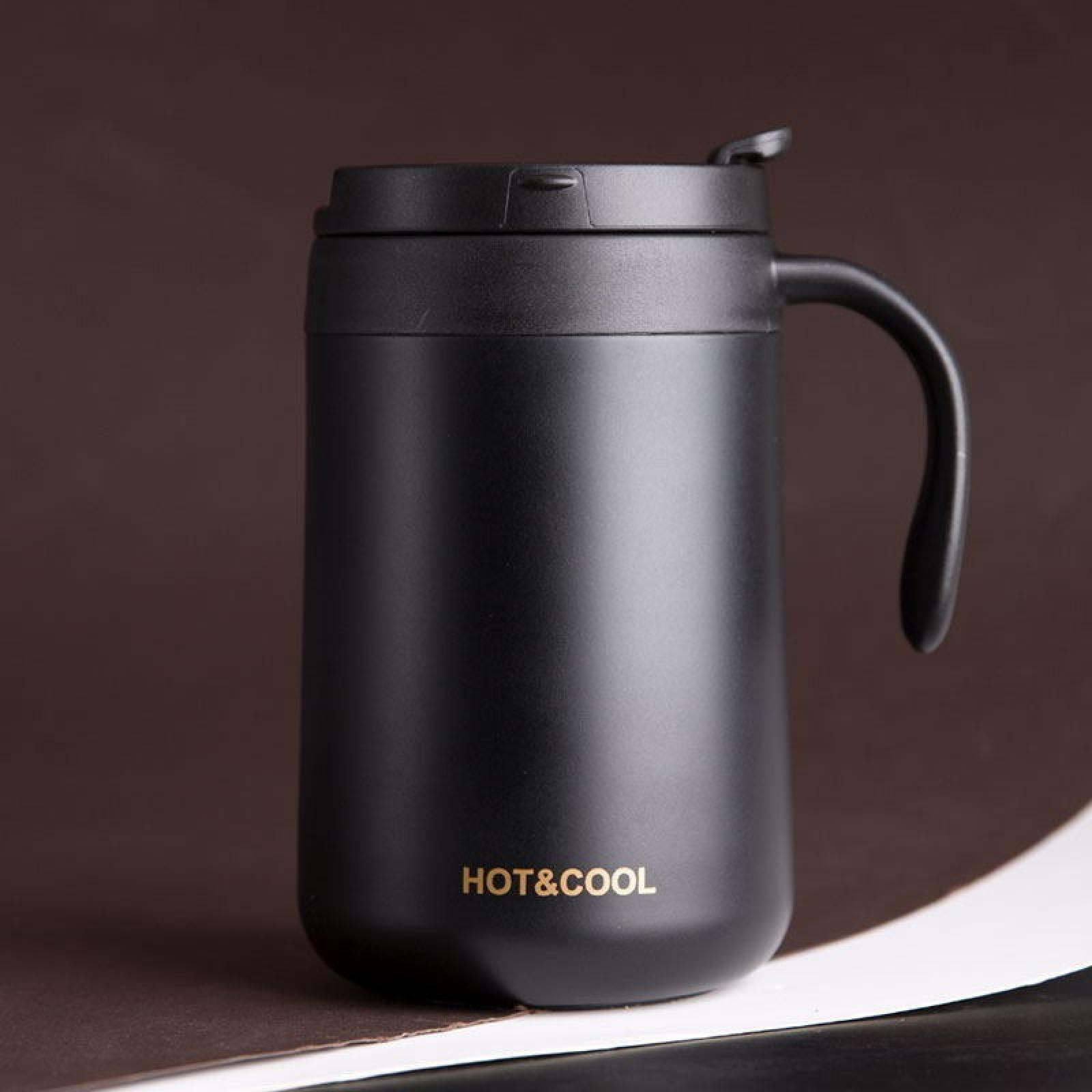 Schwarzer Reisebecher mit Henkel, Deckel und Schriftzug 'HOT&COOL'. Auf braunem und weißem Hintergrund.